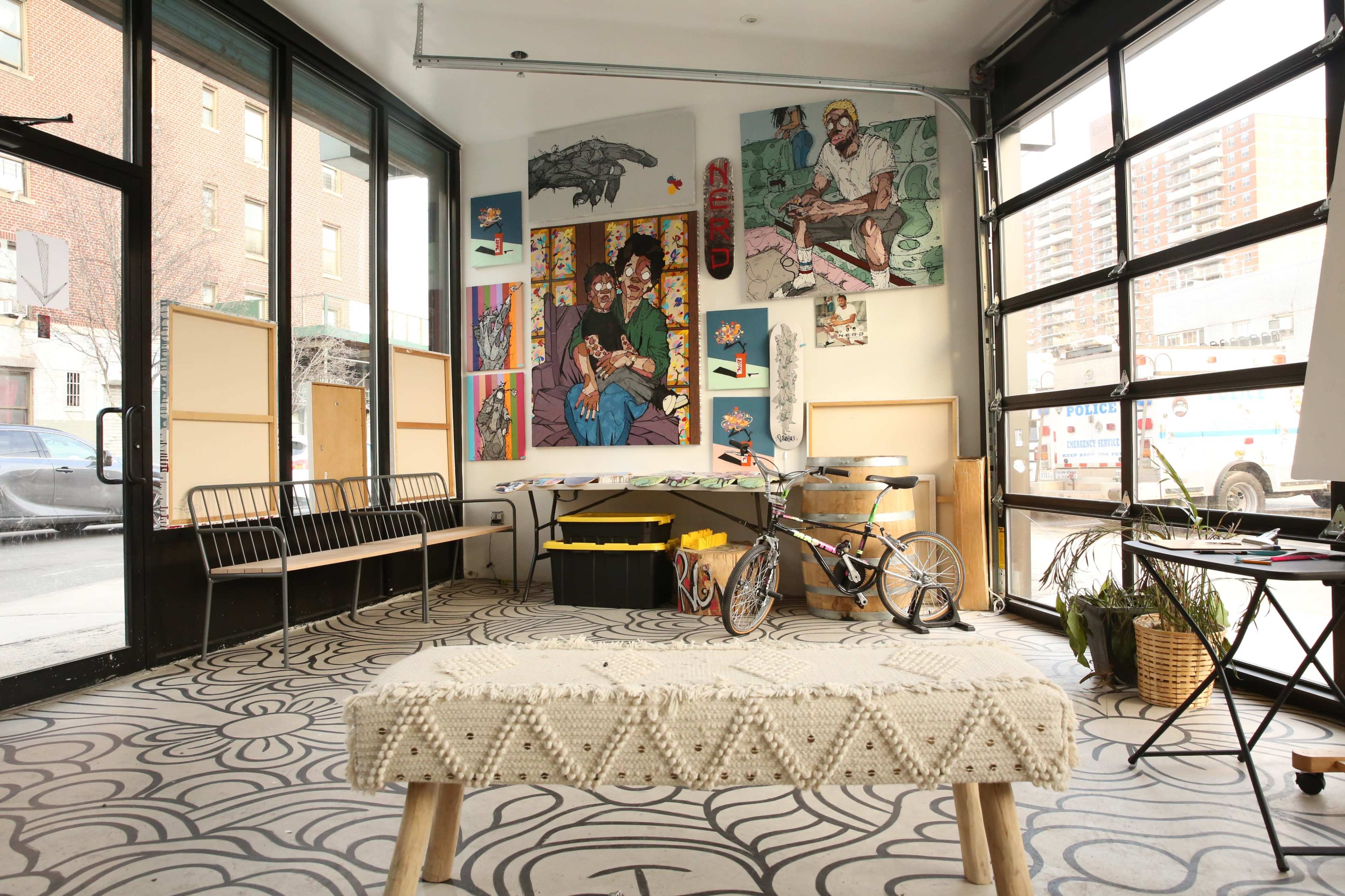 An art-filled room with large windows, a bicycle, and a bench, featuring a patterned floor and various artworks on the walls.