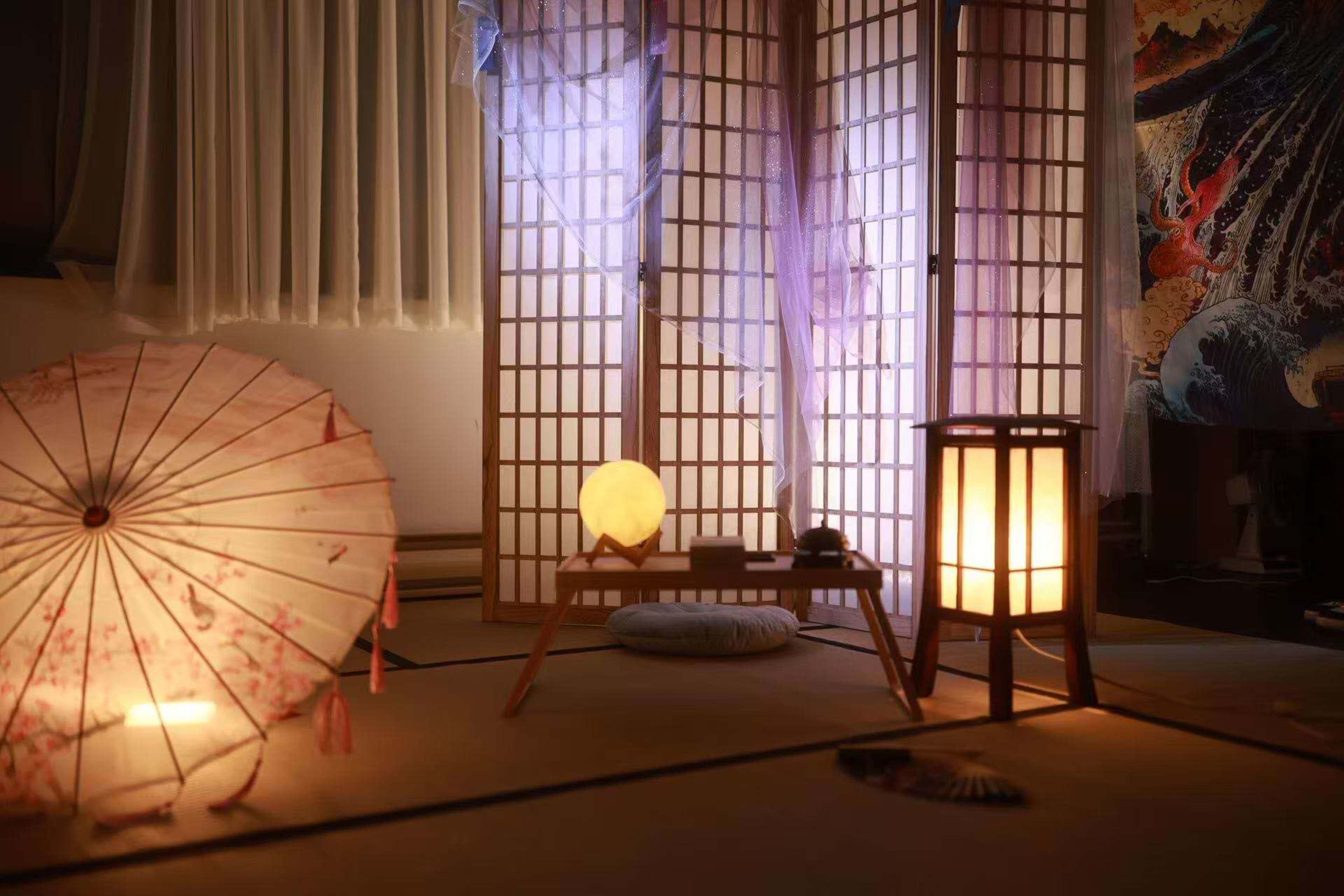 The scene features a serene room with a shoji screen, a table with a round glowing lamp, a traditional parasol, and softly lit lanterns on a tatami mat floor.