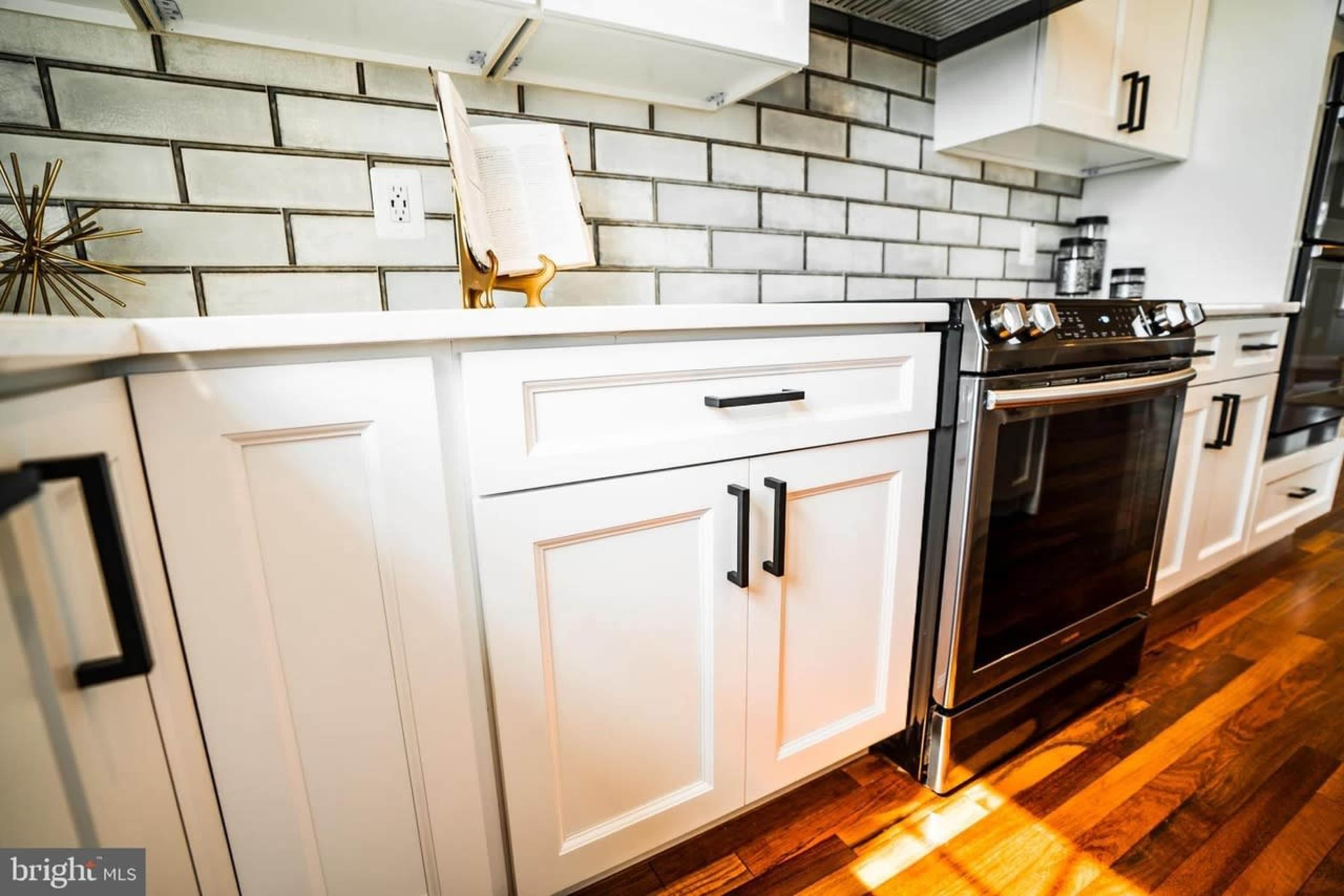 The image shows a modern kitchen with white cabinets, a stainless steel stove, and gray tiled backsplash.