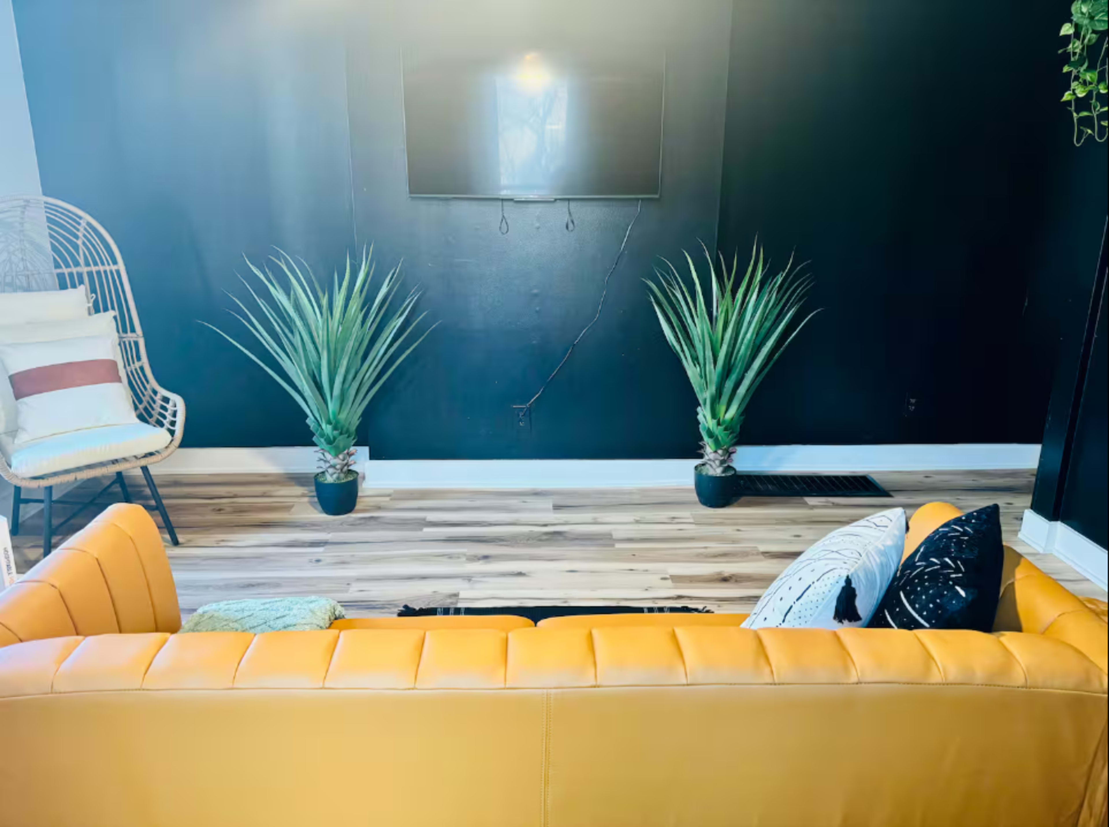 A yellow couch faces a dark wall with two potted plants on either side and a television mounted above.