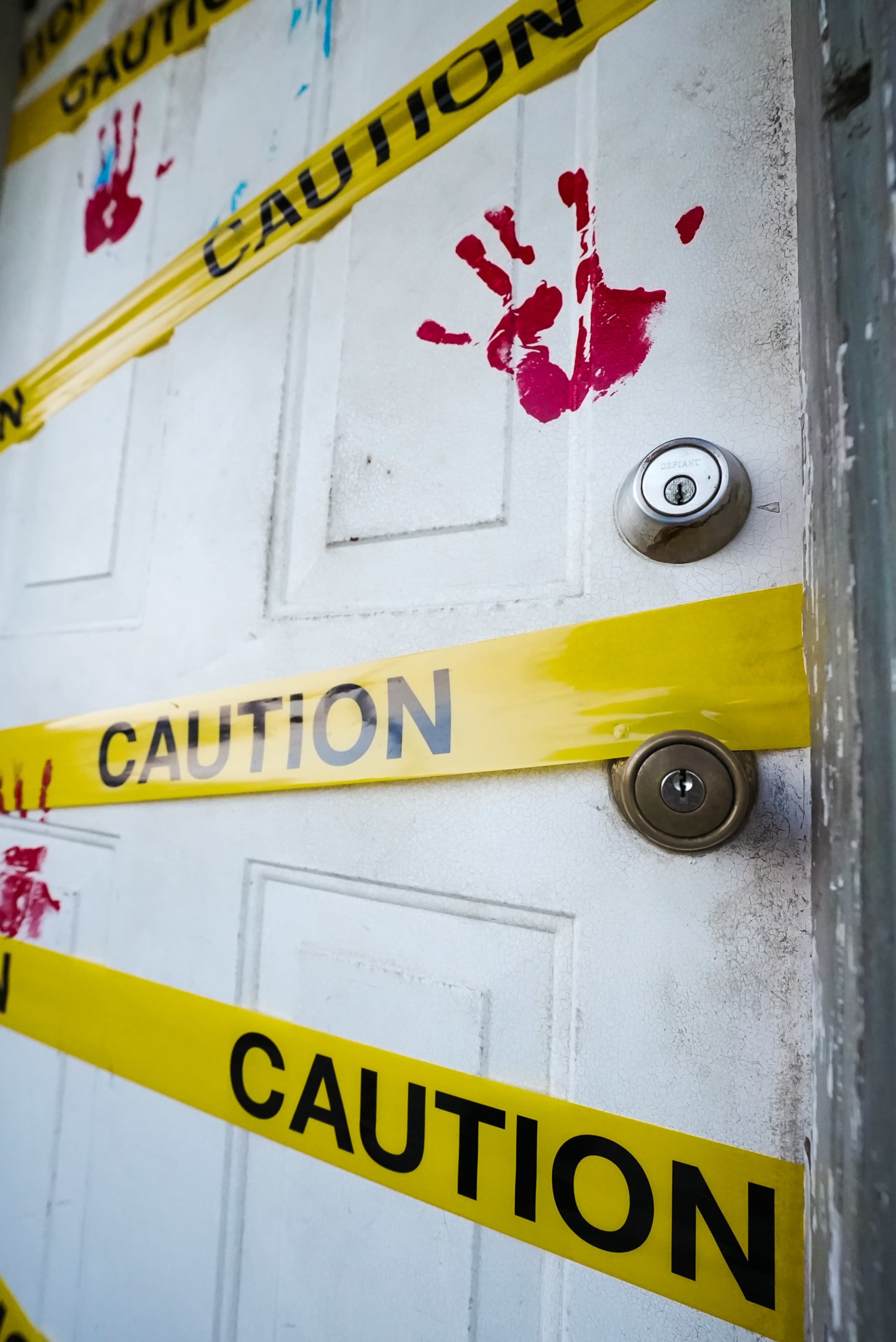 A door is sealed with yellow caution tape and marked with red handprints.