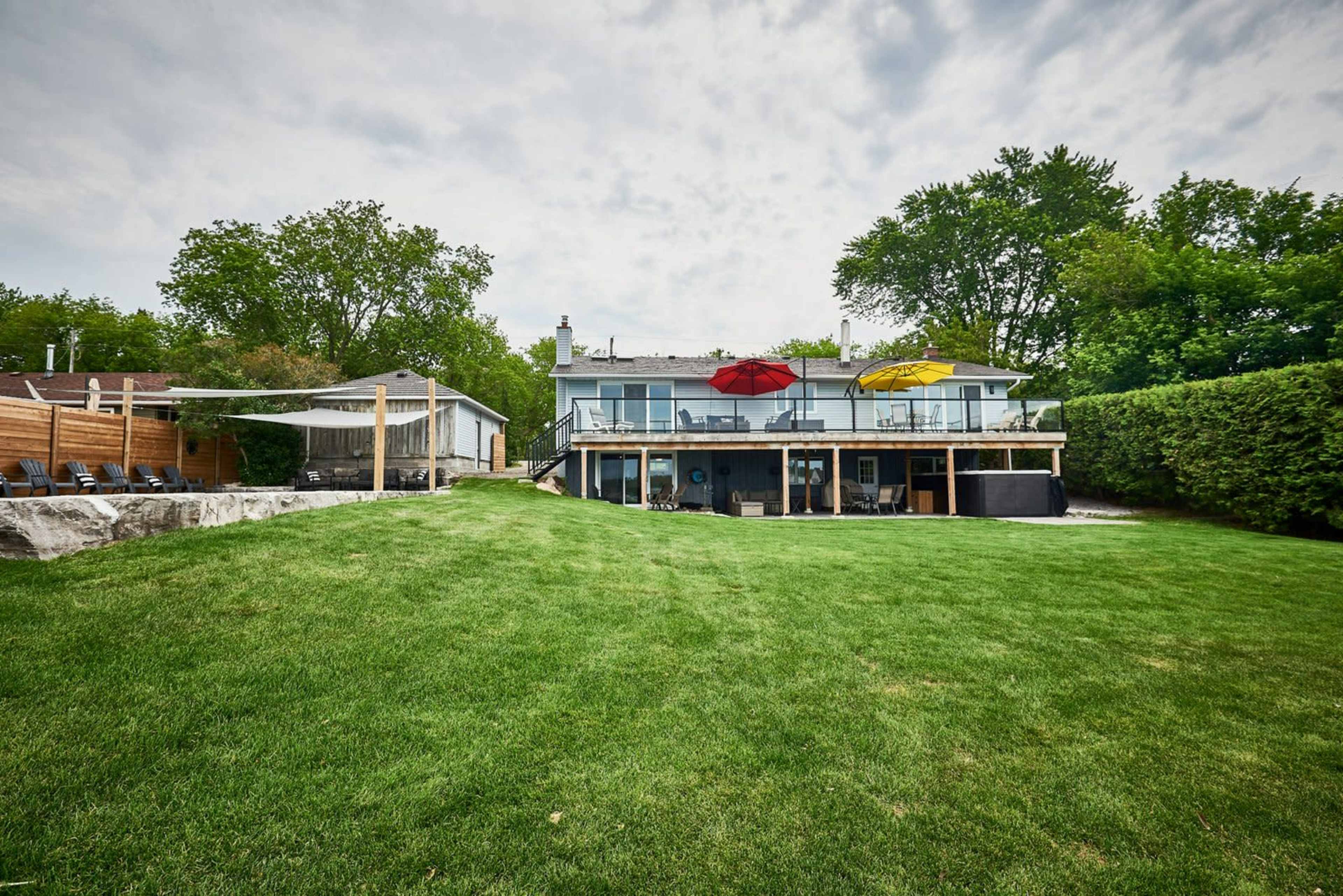 A spacious backyard with a well-maintained lawn, a two-story house featuring upper decks with red and yellow umbrellas, and a small outbuilding nearby.