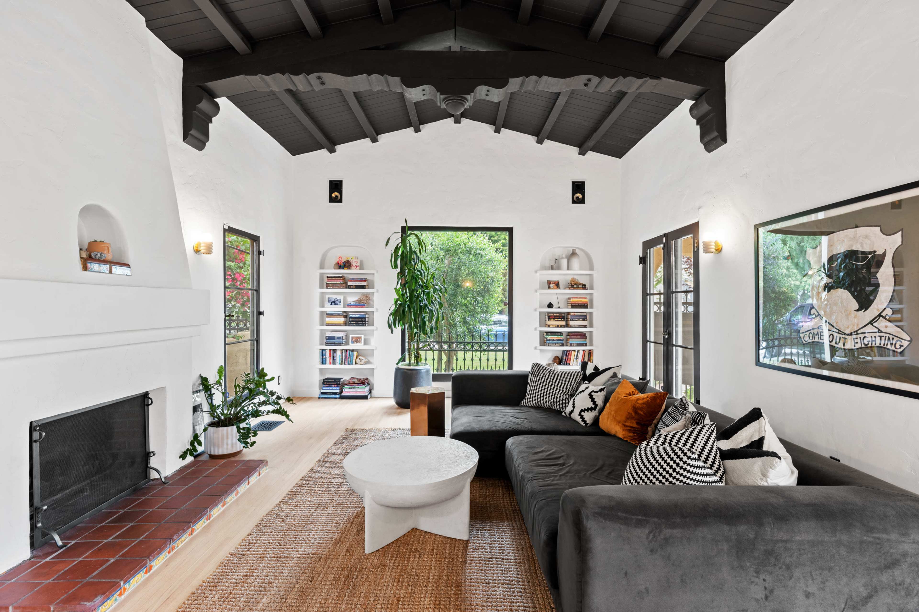 The living room features a large gray sectional sofa, a circular white coffee table, and built-in shelves filled with books, all set against a backdrop of white walls and a vaulted ceiling.