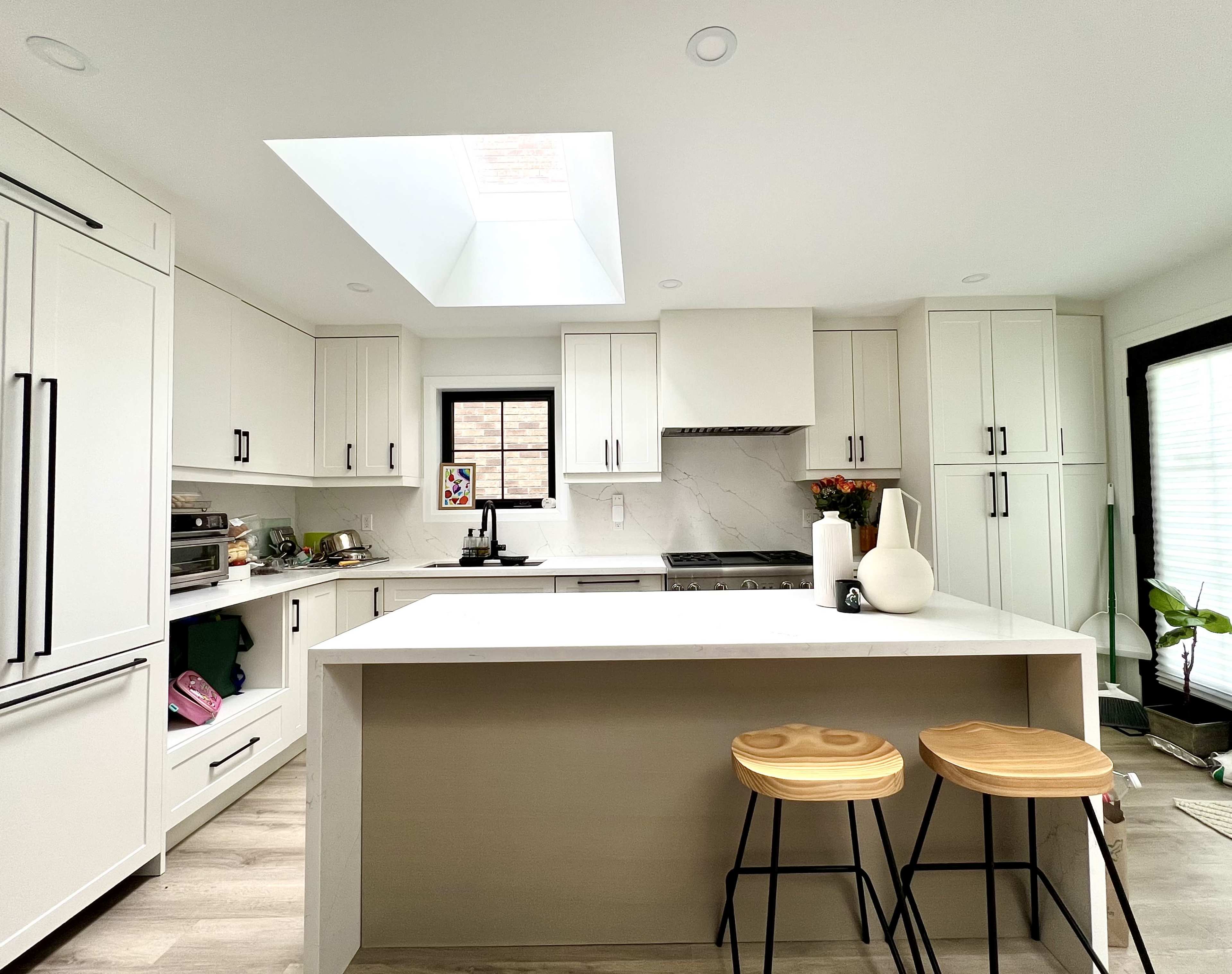 The image shows a modern kitchen with white cabinets, a large island, and two wooden bar stools.