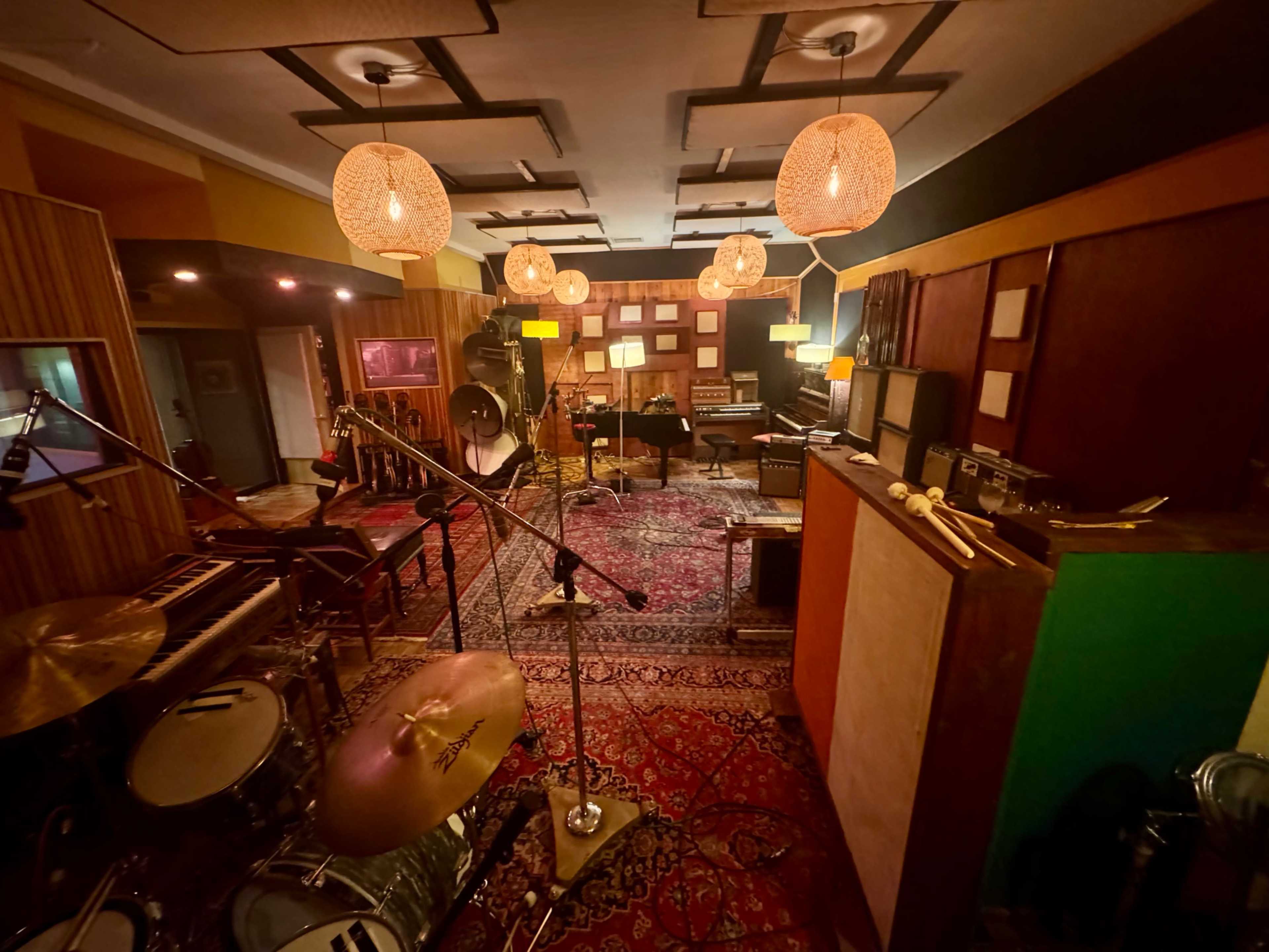 The image shows a recording studio featuring musical instruments, microphones, and warm lighting, with a vibrant area rug covering the floor.