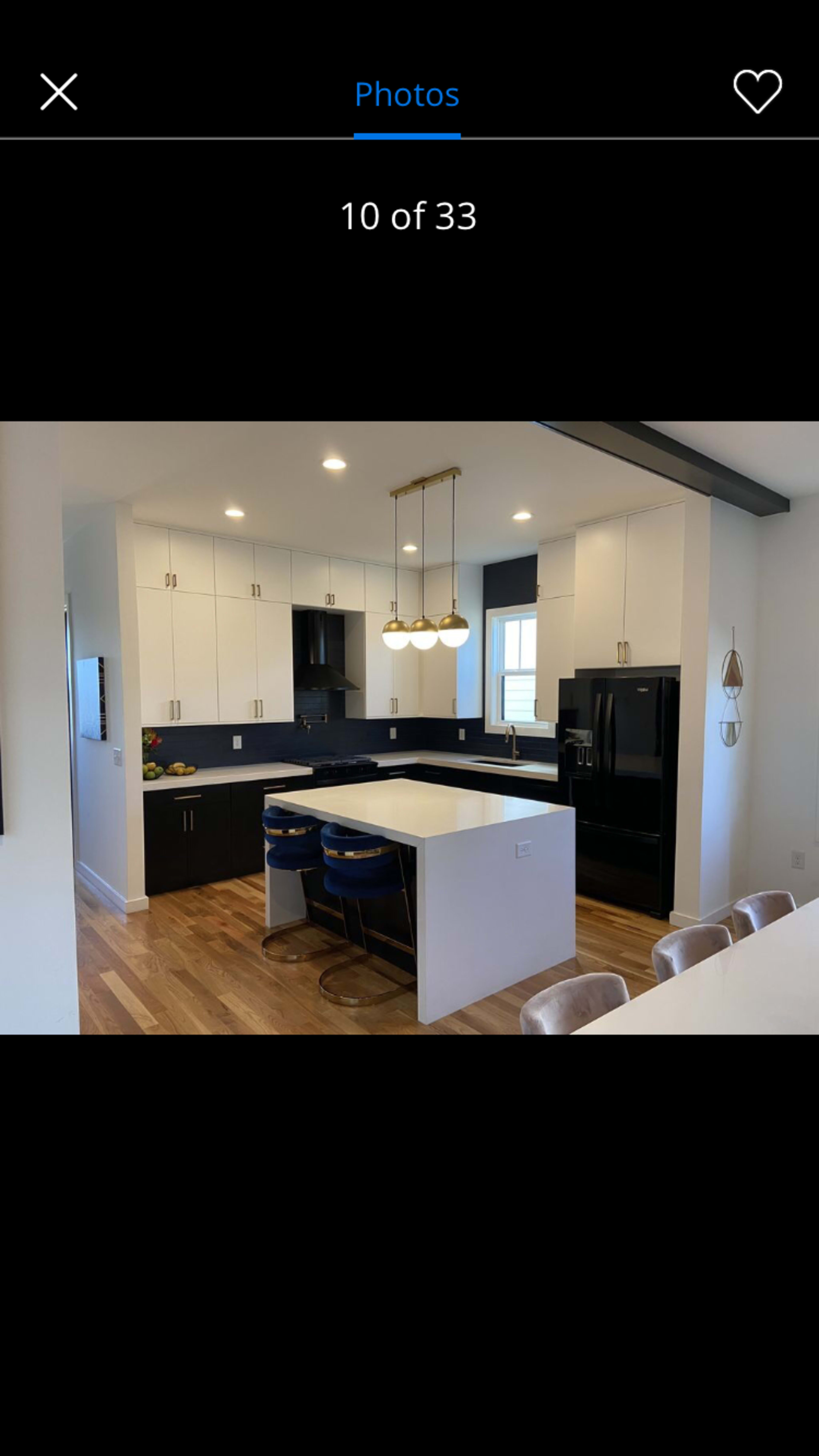 A modern kitchen featuring a mix of black and white cabinetry, a central island with seating, and pendant lighting overhead.