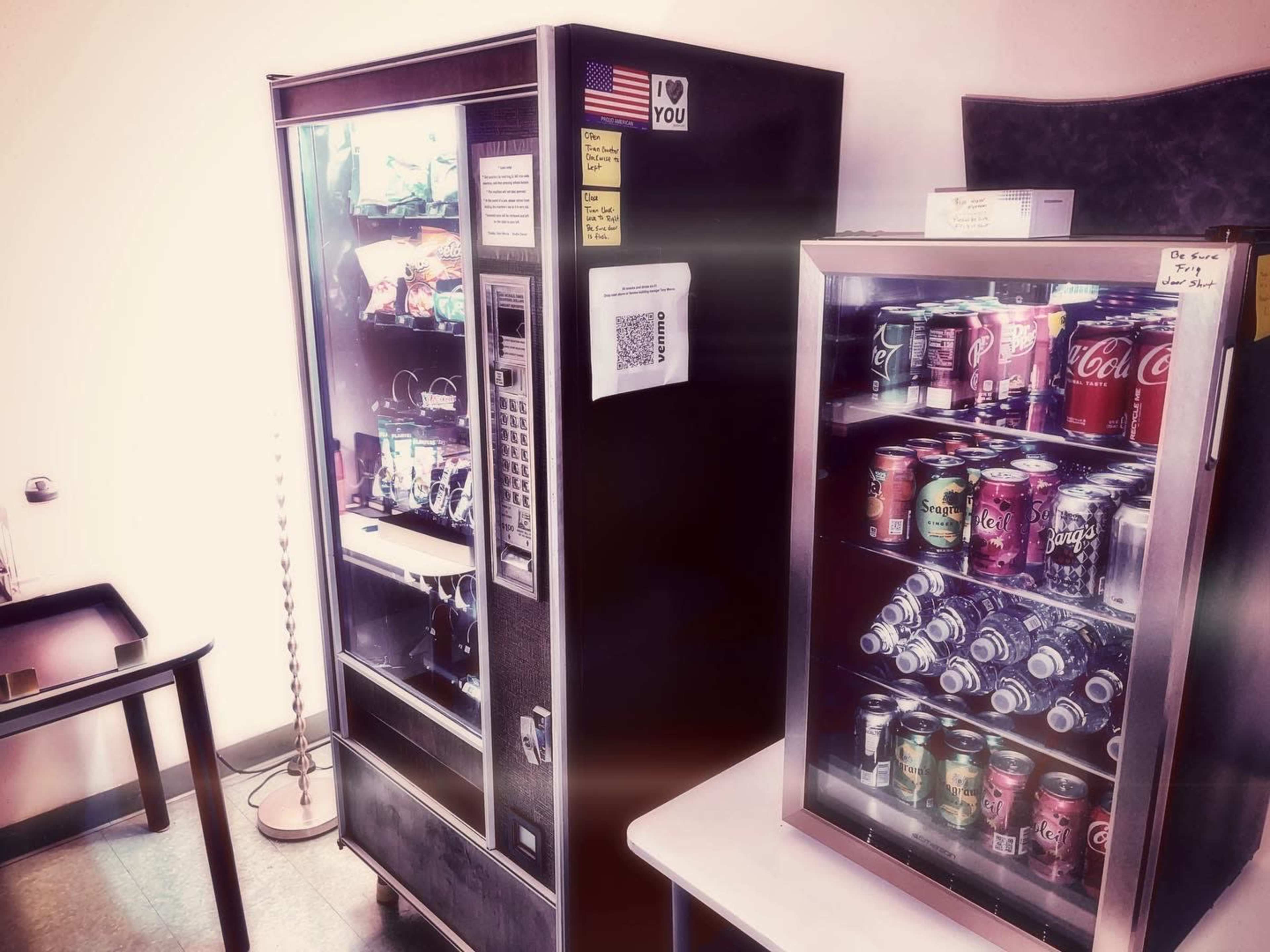 The image shows two vending machines in a room, one stocked with snacks and drinks, and the other primarily filled with cans of soda.