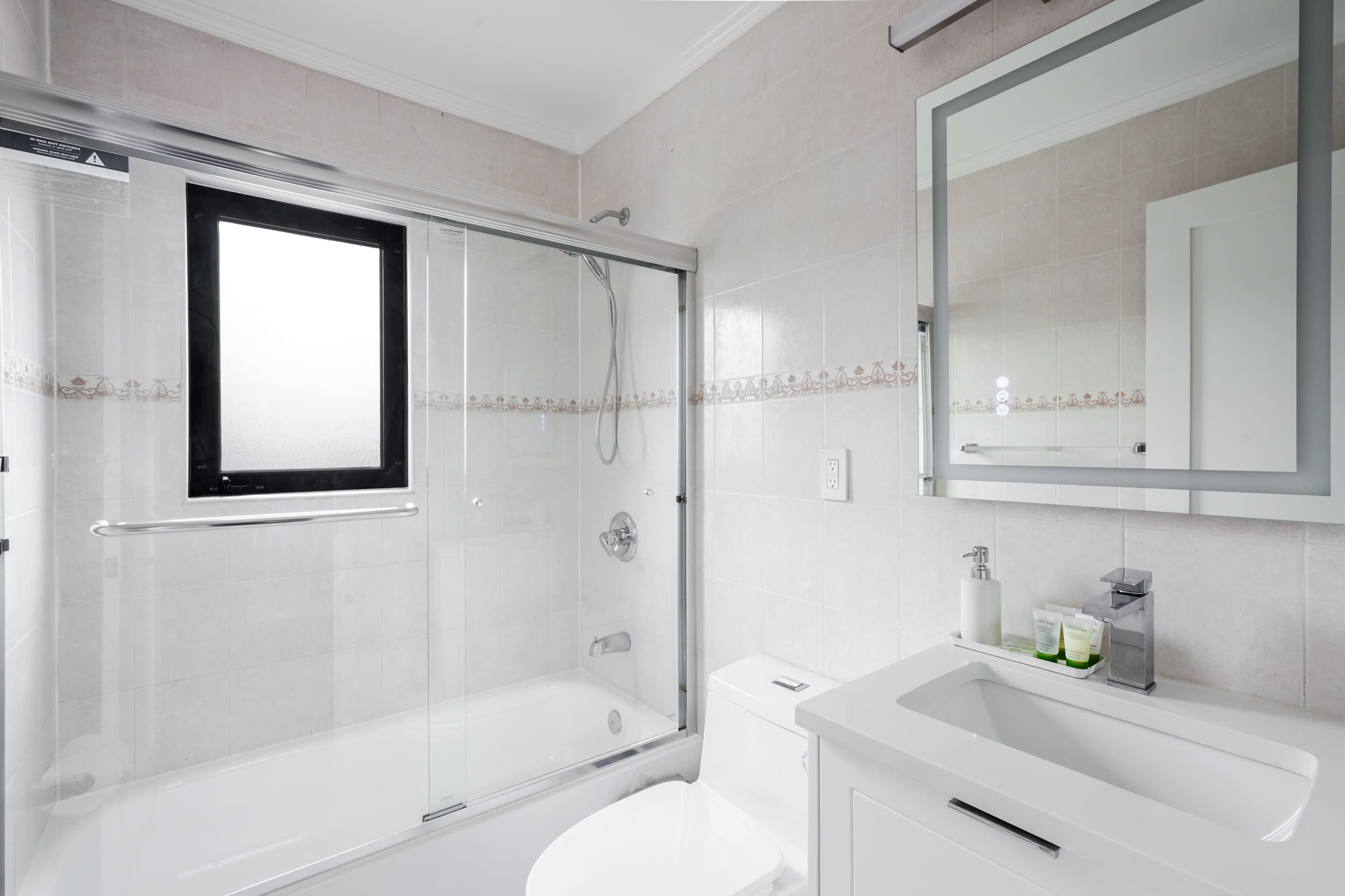 A modern bathroom featuring a glass-enclosed shower, a bathtub, a white vanity with a mirror, and a window.