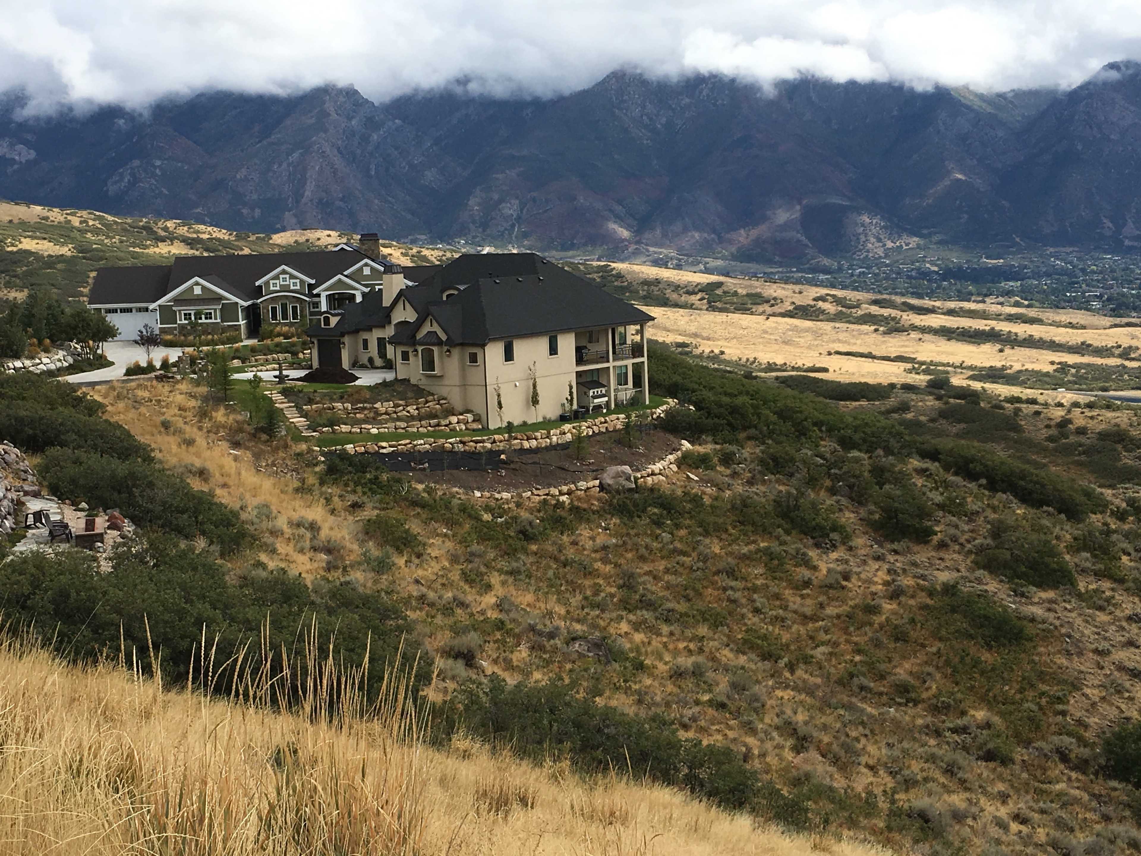 A cluster of homes is situated on a hillside, overlooking a valley with mountains in the background under a cloudy sky.
