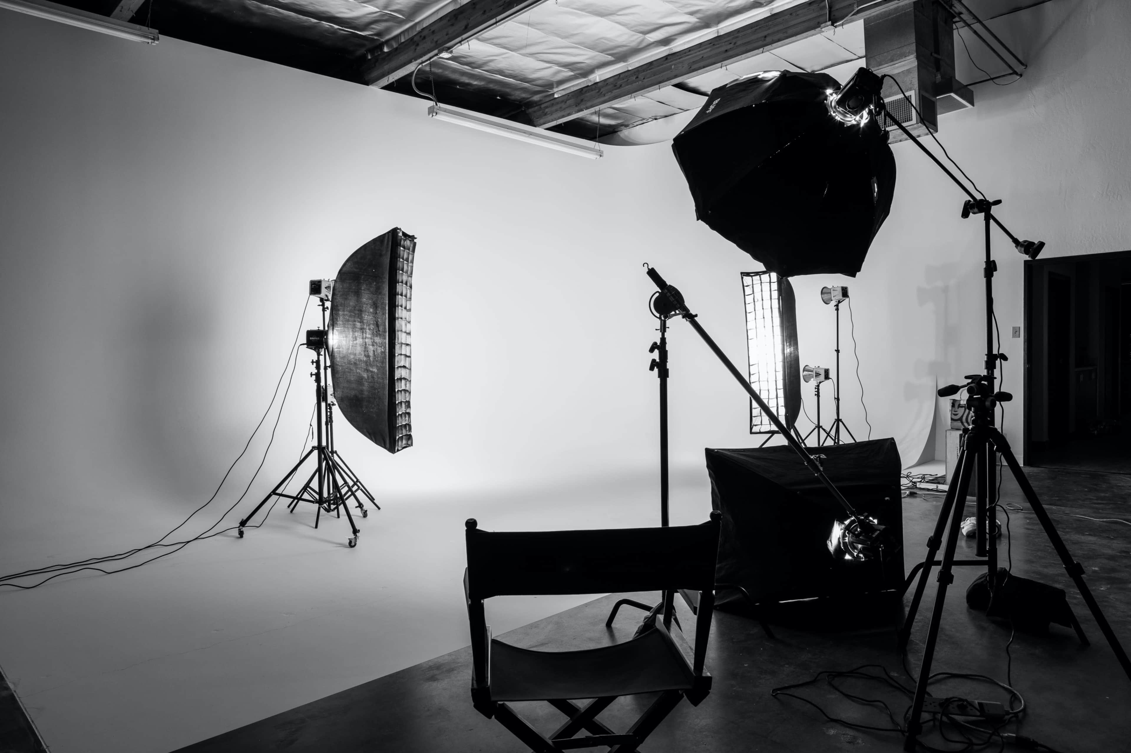 An empty photography studio setup with various lighting equipment and a director's chair positioned in front of a plain backdrop.