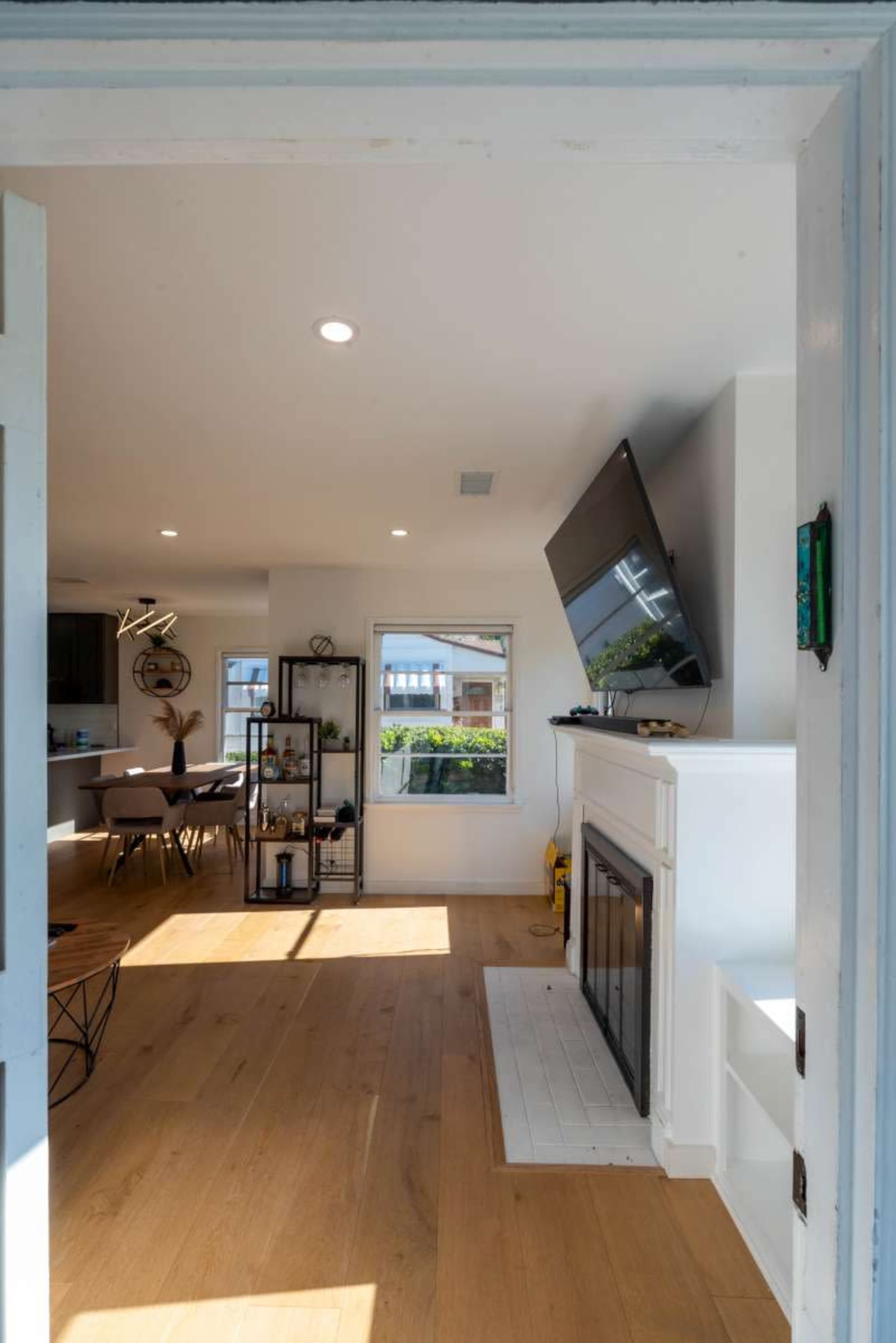 An open doorway leading into a modern living room featuring a fireplace, a TV mounted on the wall, and a view of the outdoors through a window.