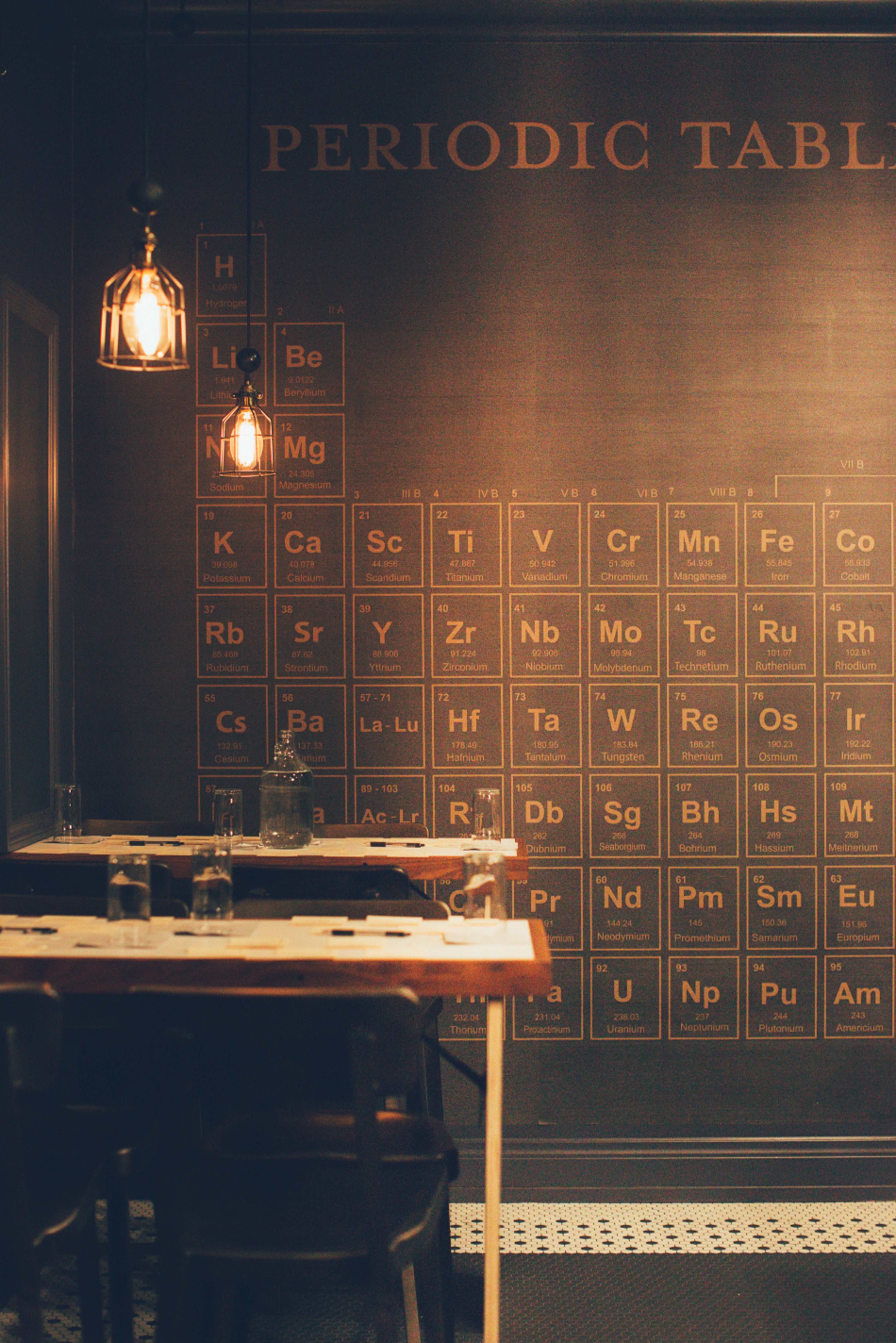 A restaurant interior with a wall featuring a periodic table of elements and tables set with glasses.