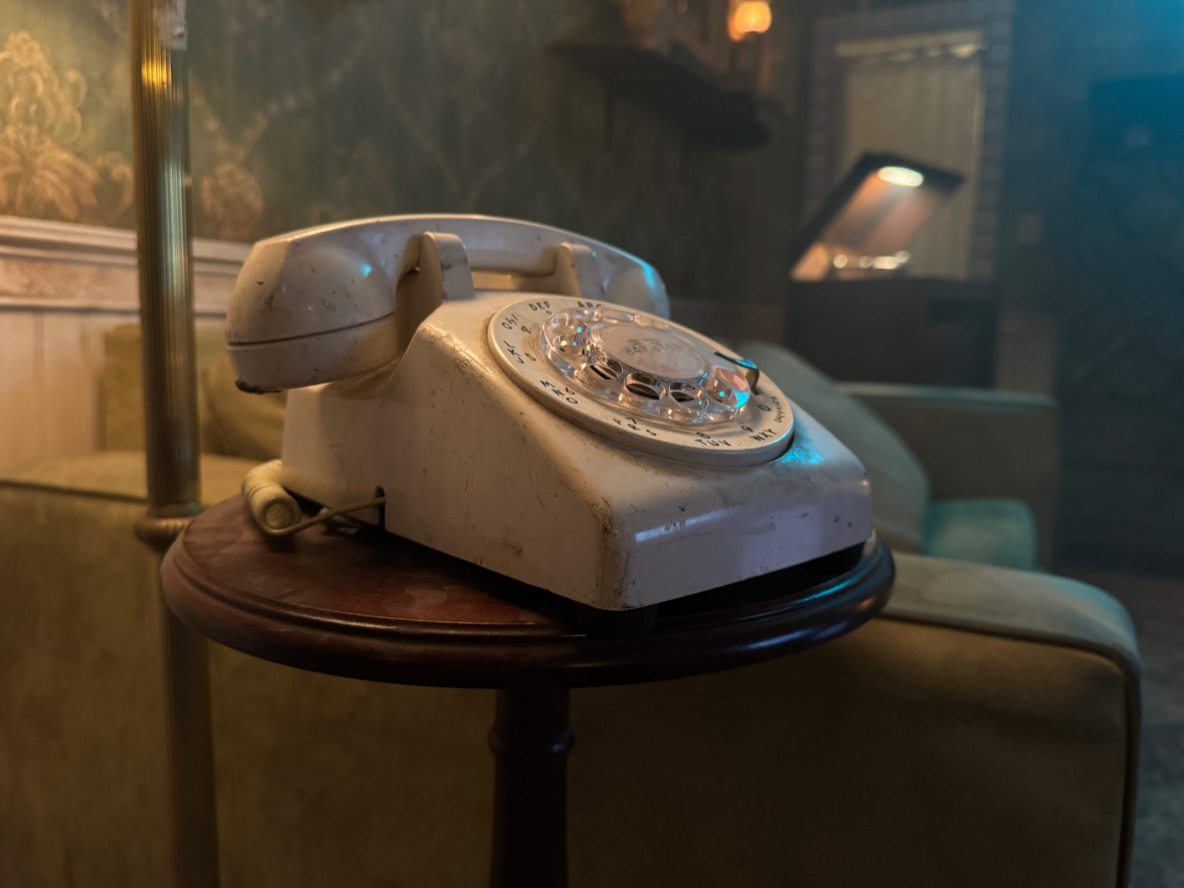 An old rotary telephone rests on a wooden table in a dimly lit room with vintage decor.