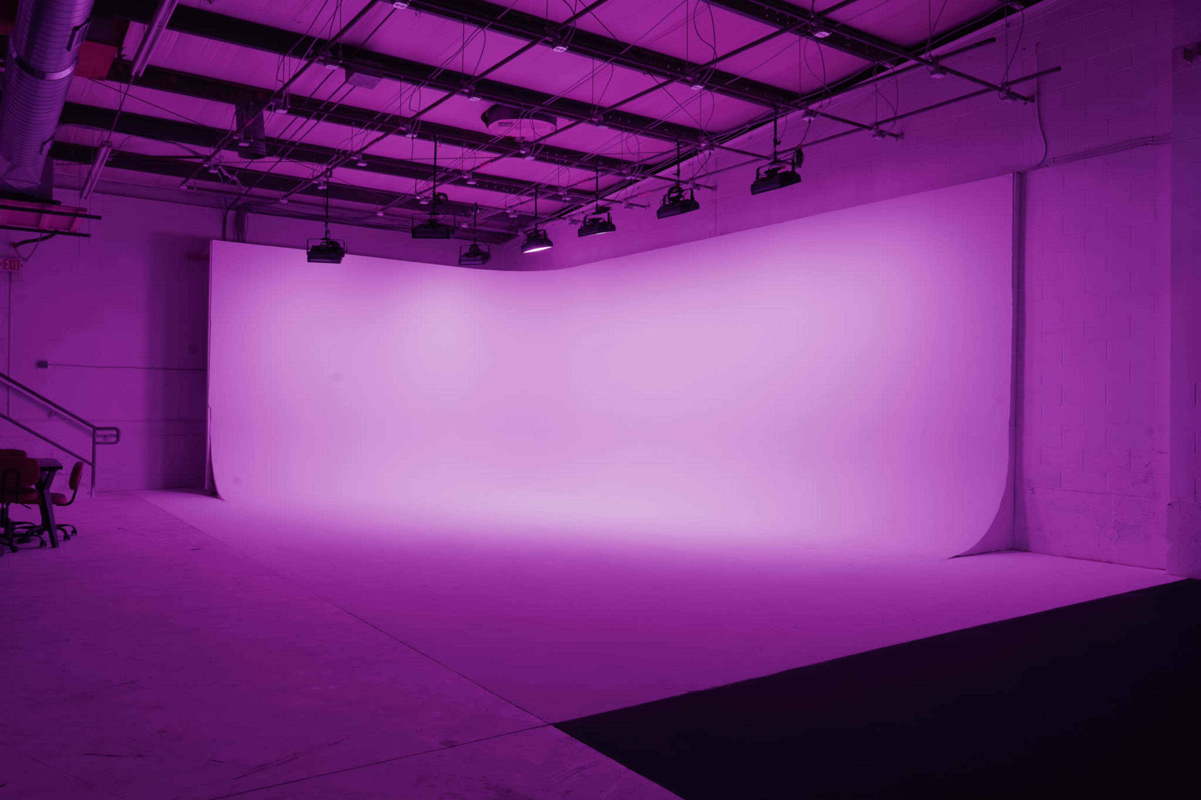 The image shows a spacious studio with a large, seamless purple backdrop and overhead lighting.