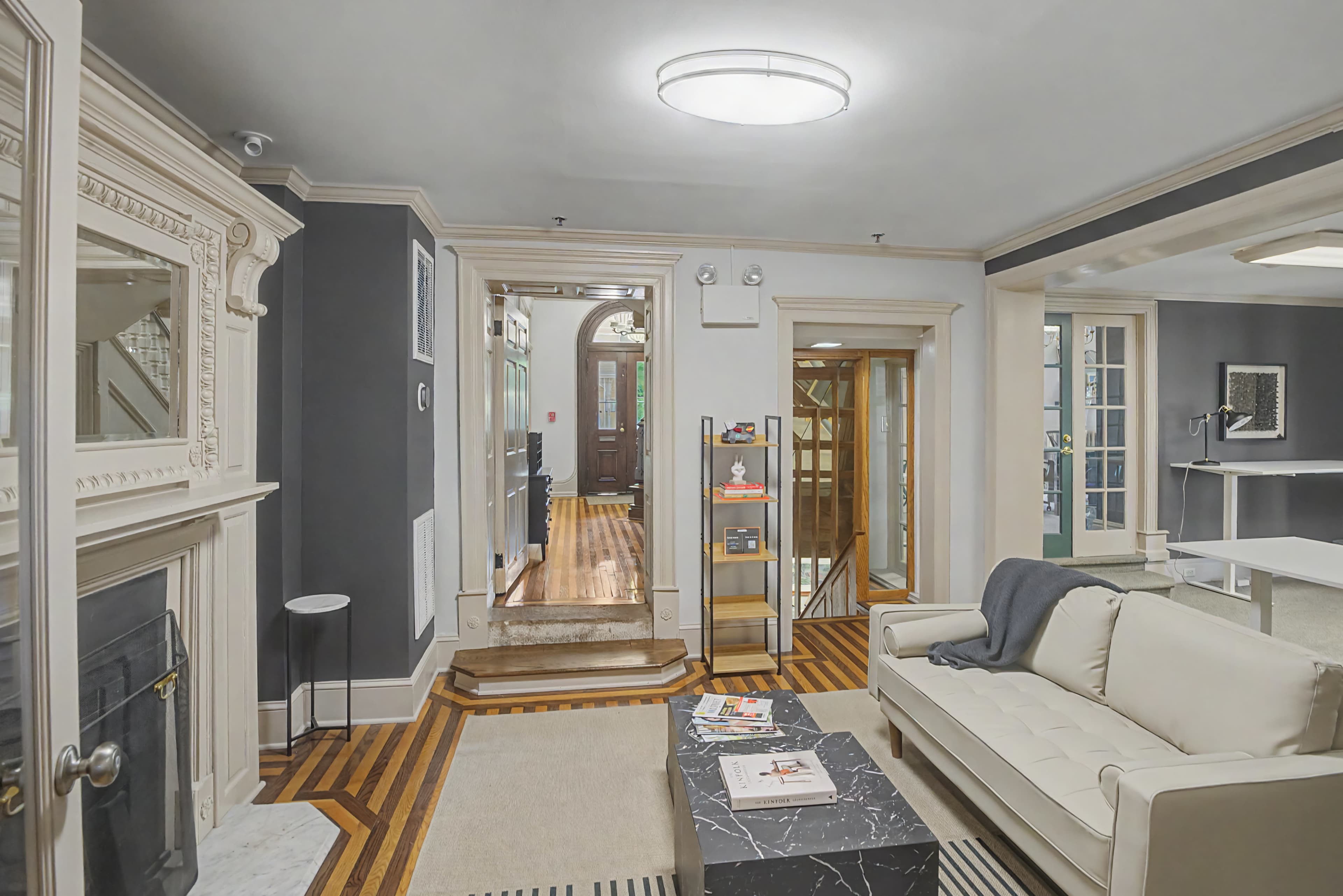 The image shows a modern living space with a white sofa, a coffee table on a rug, and decorative elements against a backdrop of elegant, dark walls and wooden flooring.