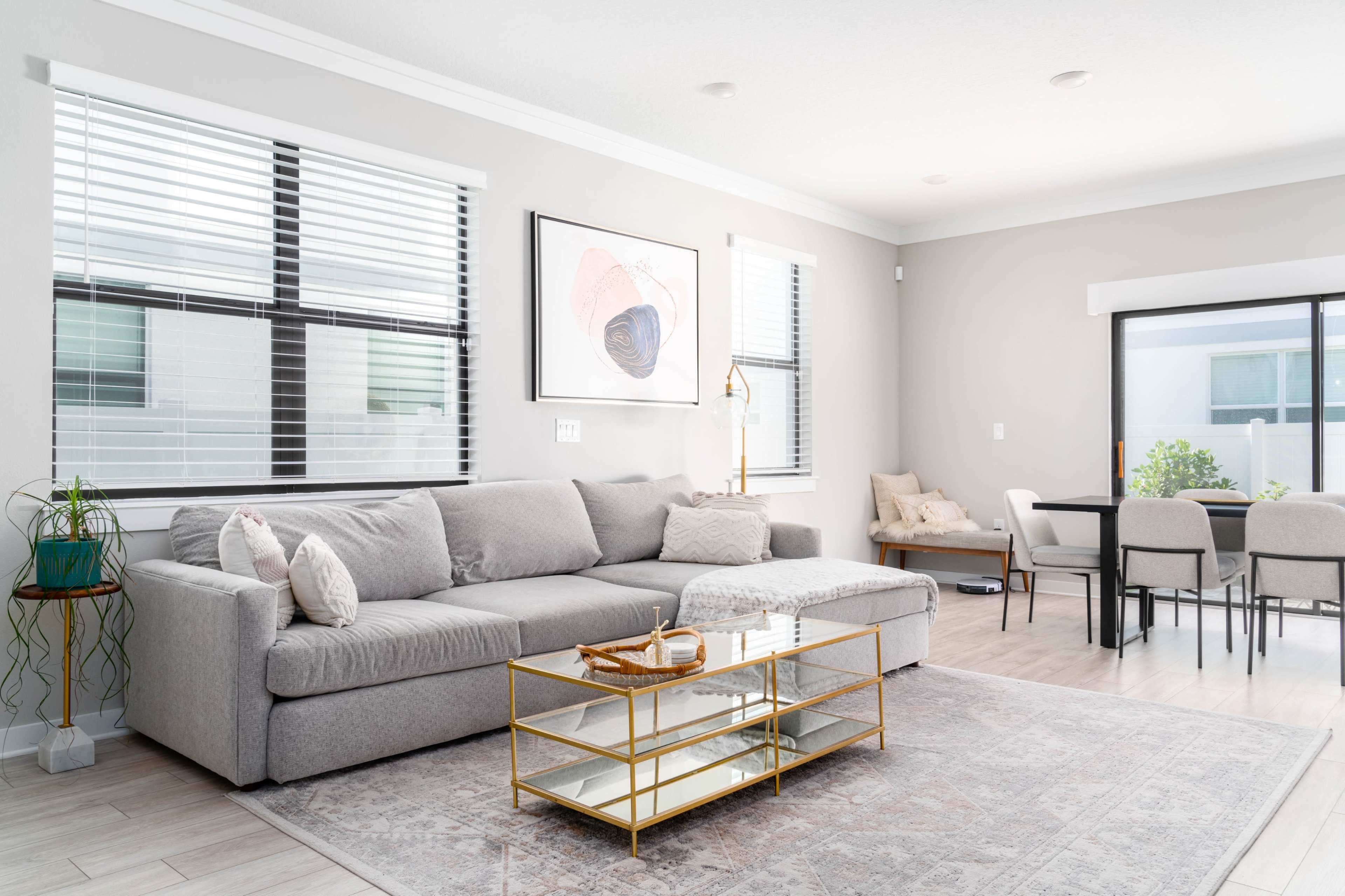 A modern living room with a gray sectional sofa, a glass coffee table, and a dining area in the background.