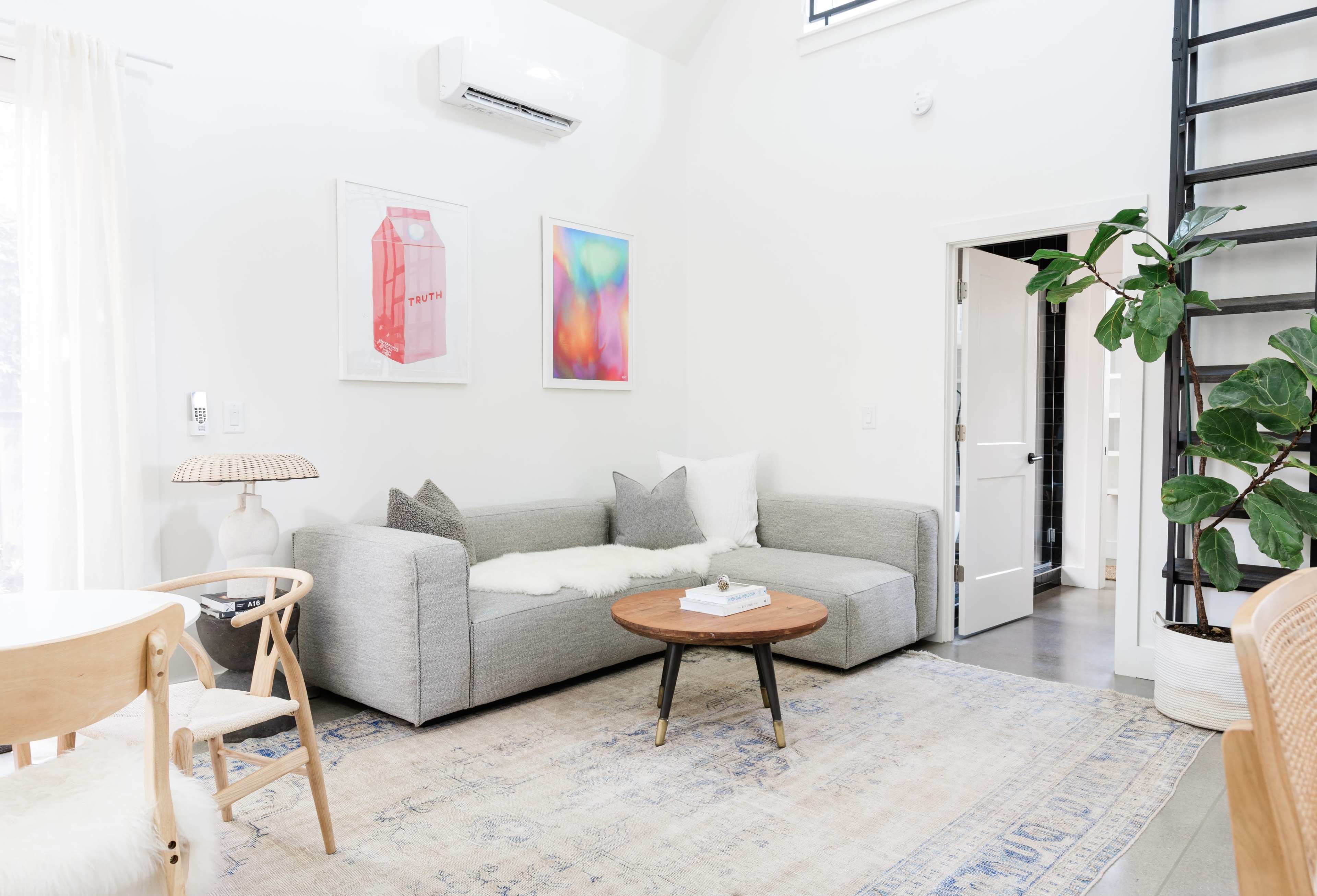 A modern living room featuring a grey sectional sofa, a round wooden coffee table, and a large plant beside a staircase.