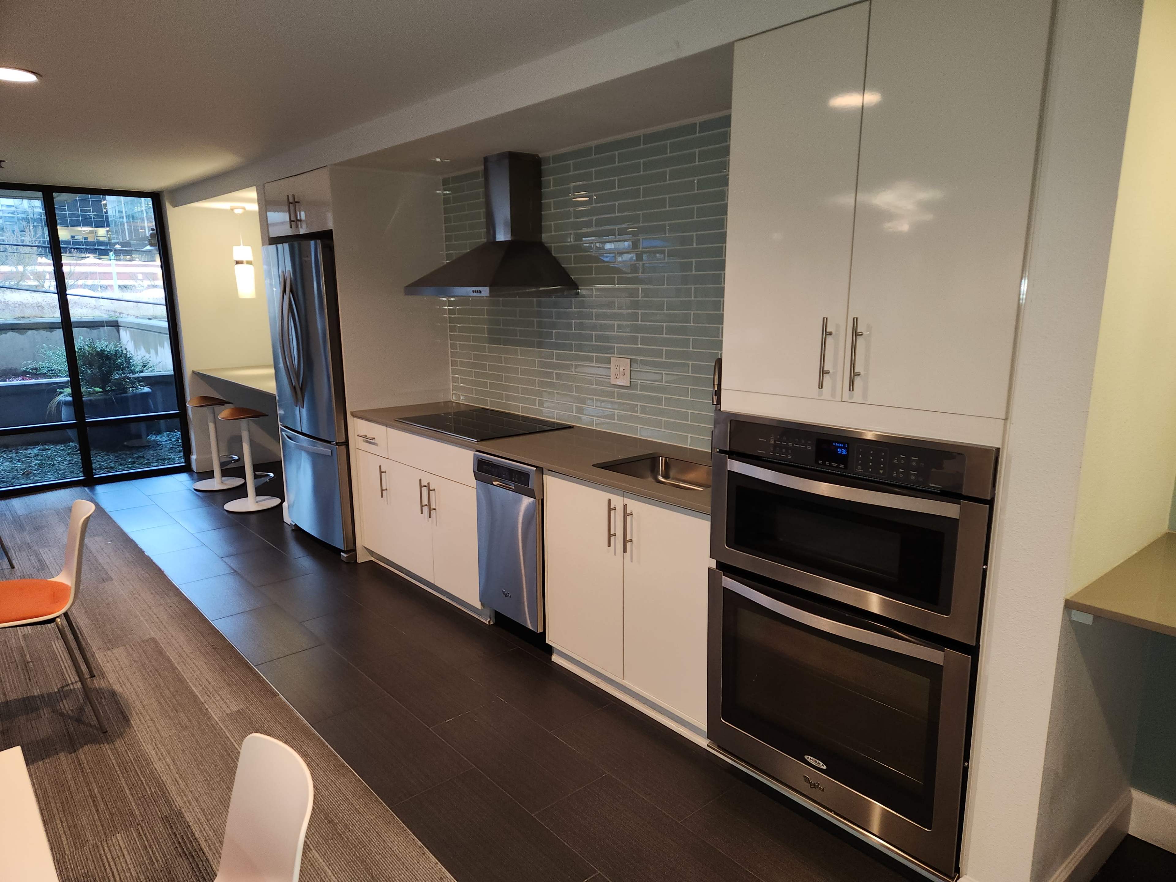 A modern kitchen with stainless steel appliances, a tiled backsplash, and white cabinetry, adjacent to a dining area with a table and chairs.