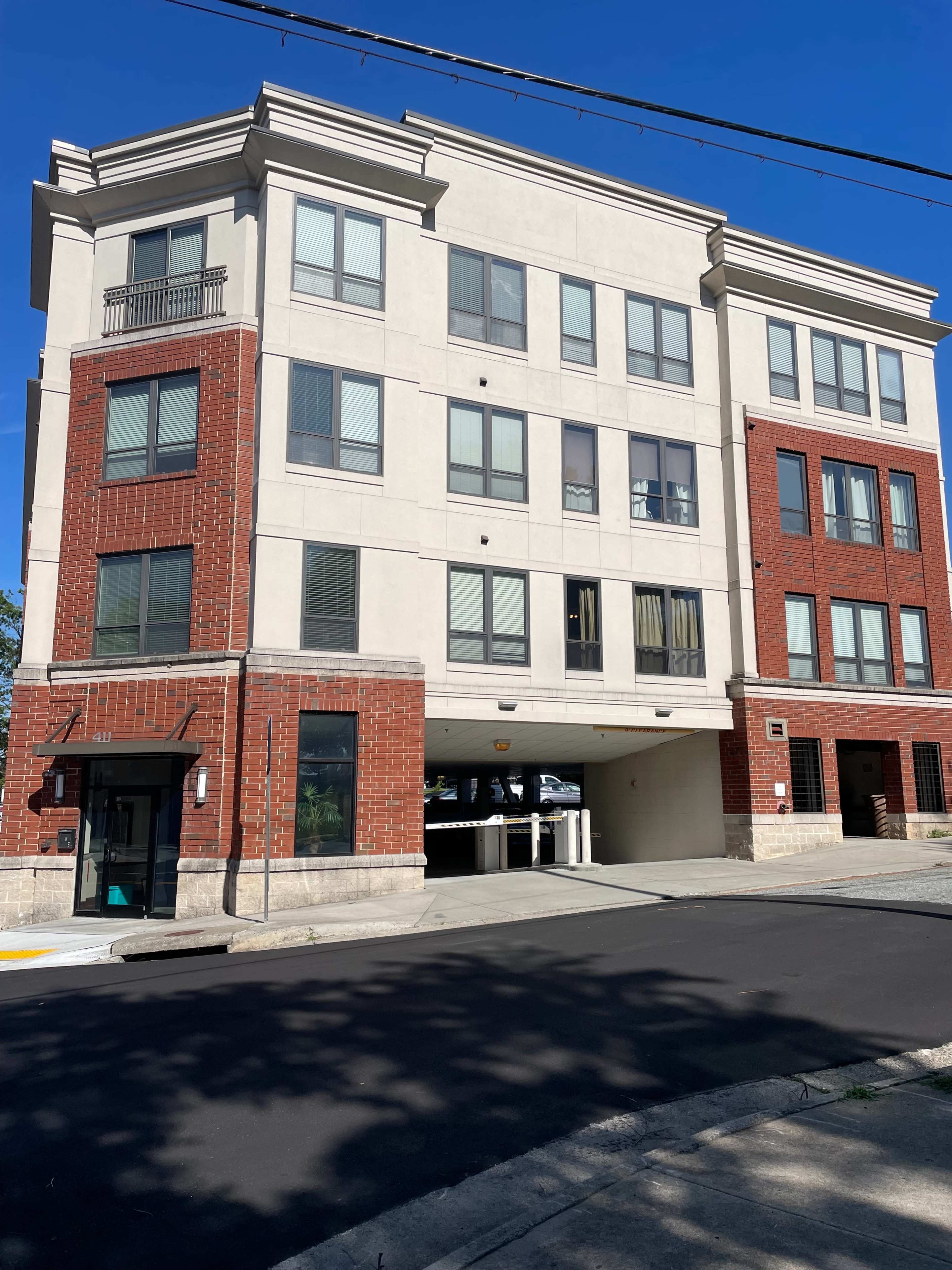 A three-story residential building features a mix of brick and stucco exteriors with parking access underneath.