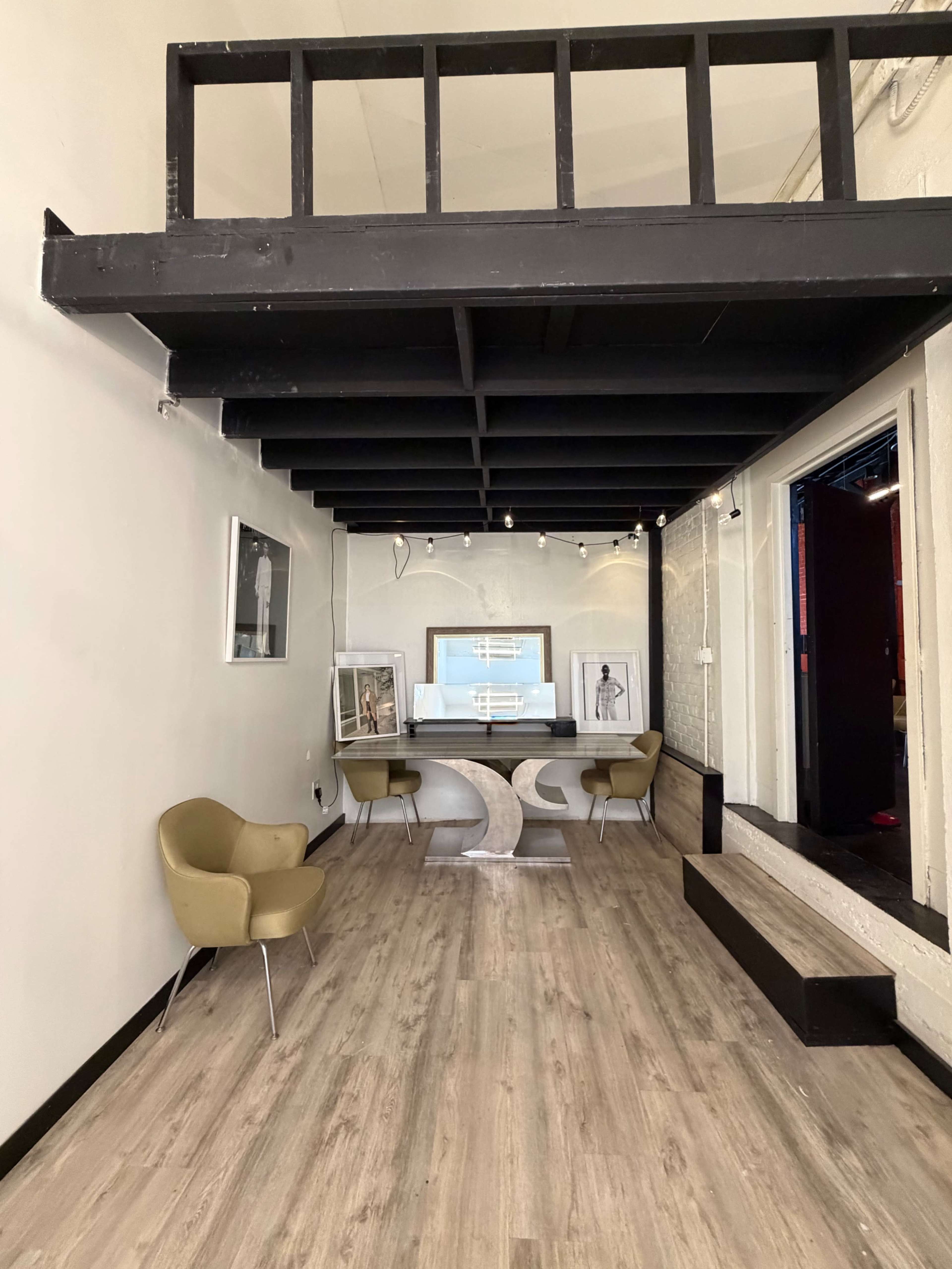 The image depicts a modern interior space featuring a minimalist reception area with a curved desk, two yellow chairs, and a lofted ceiling supported by black beams.