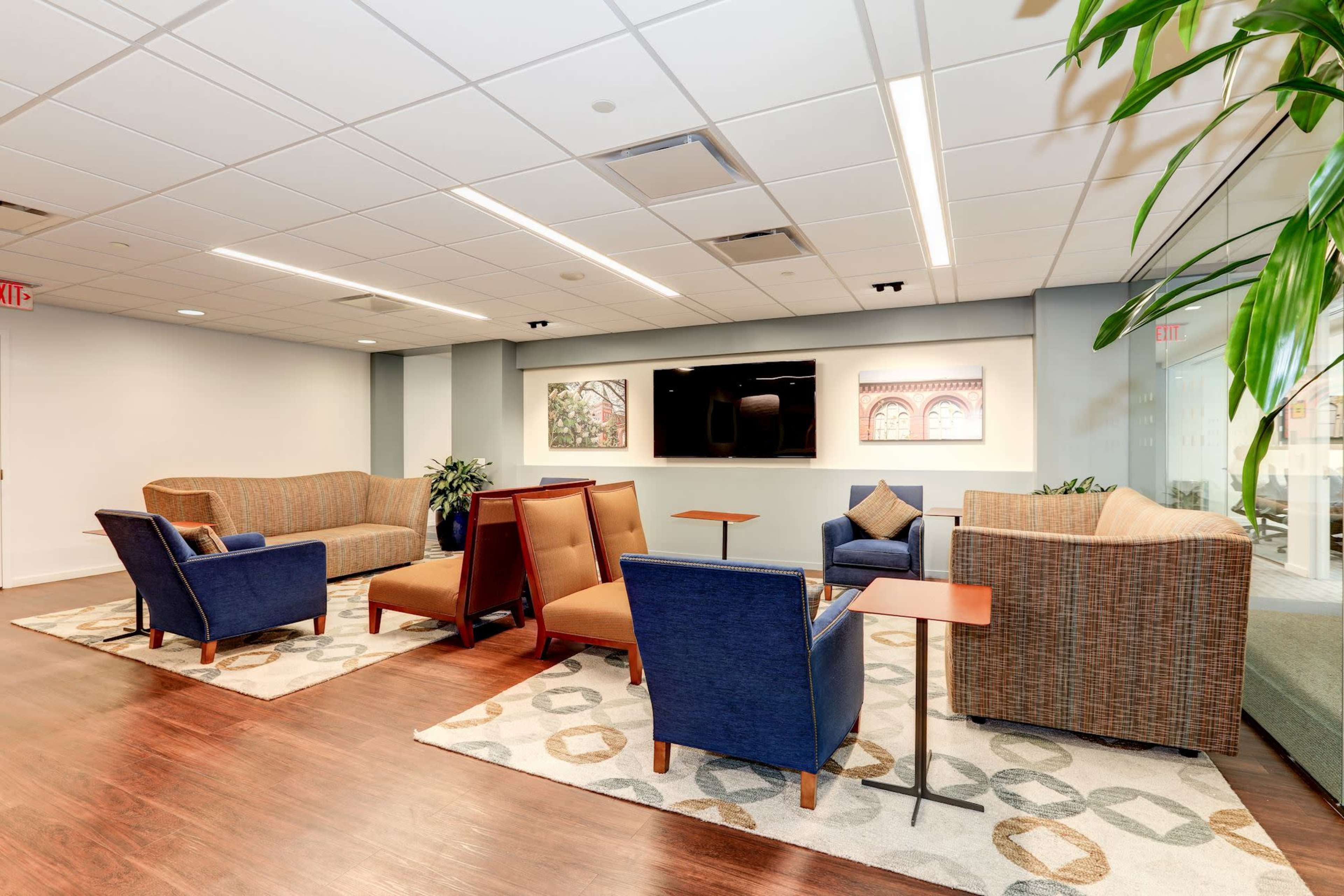 A modern lounge area furnished with patterned rugs, seating arrangements of chairs and sofas, and a large television mounted on the wall.