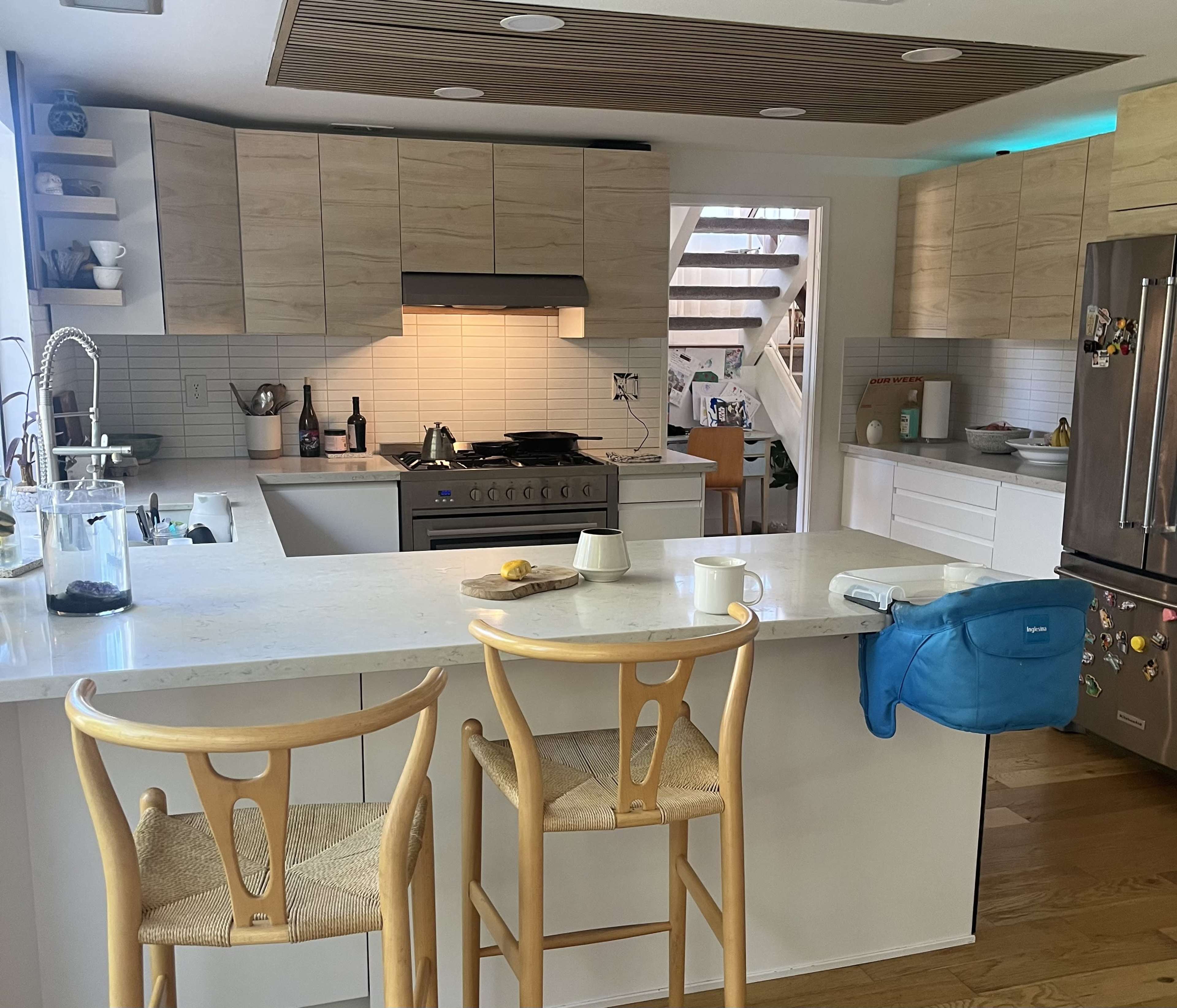 A modern kitchen with light-colored cabinetry, a central island with two wooden stools, and stainless steel appliances.