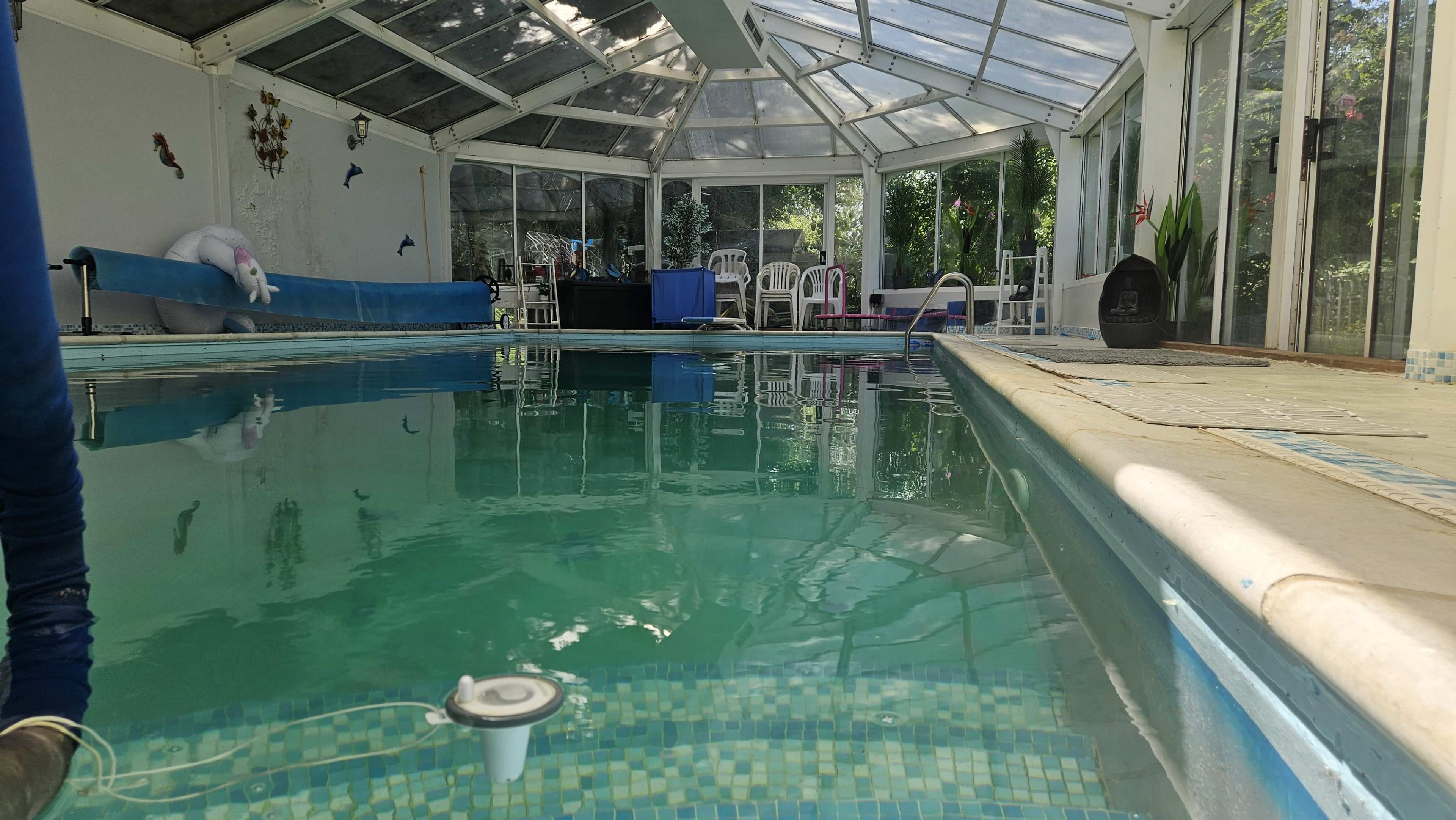 The image shows an indoor pool area with a transparent roof, seating around the pool, and a unicorn float in the water.