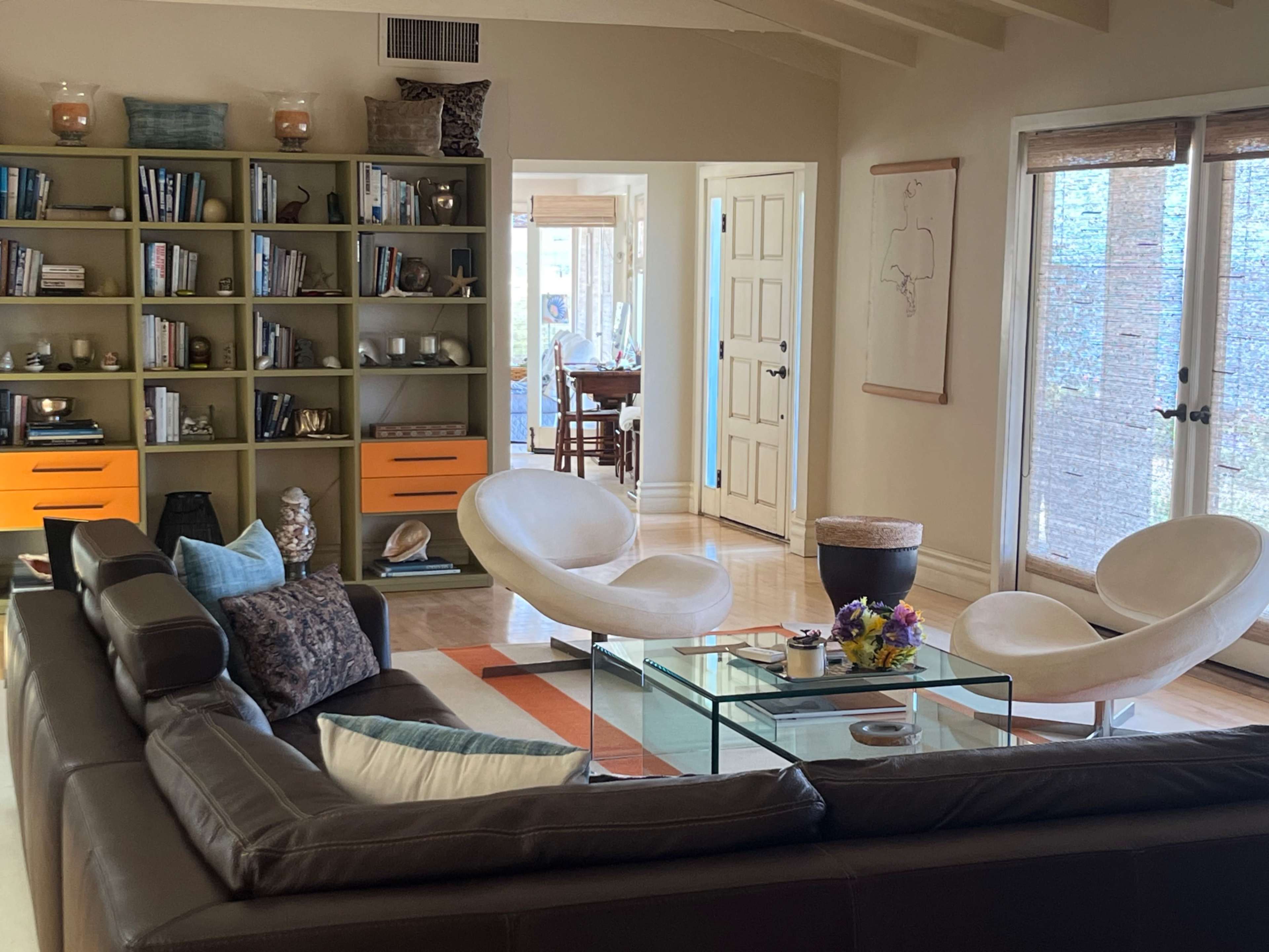 The image features a modern living room with a sectional sofa, two white chairs, a glass coffee table, and a bookshelf against the wall filled with books and decorative items.