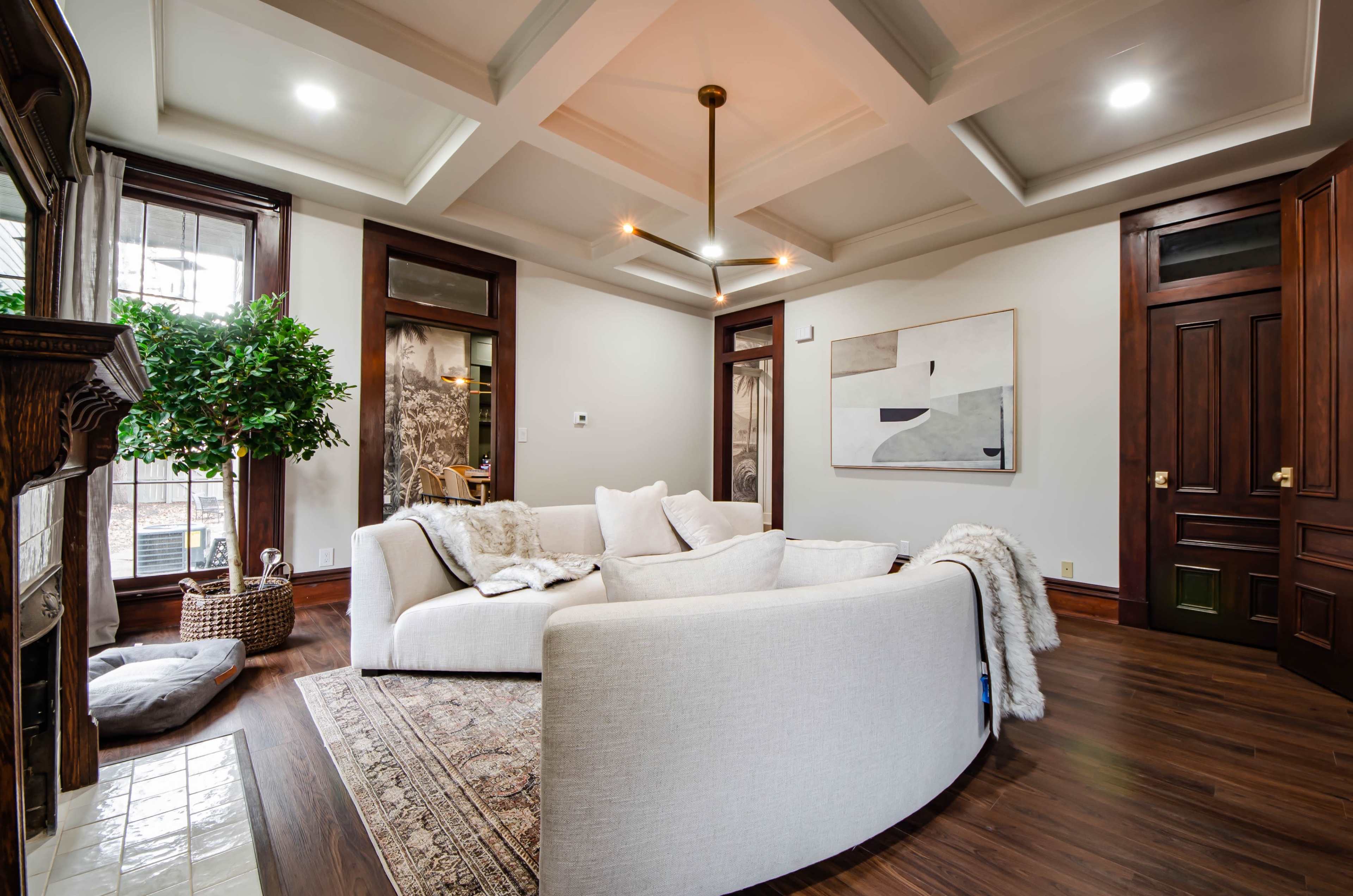 A light-colored sectional sofa in a modern living room with wooden floors, a large artwork on the wall, and a potted plant in the corner.