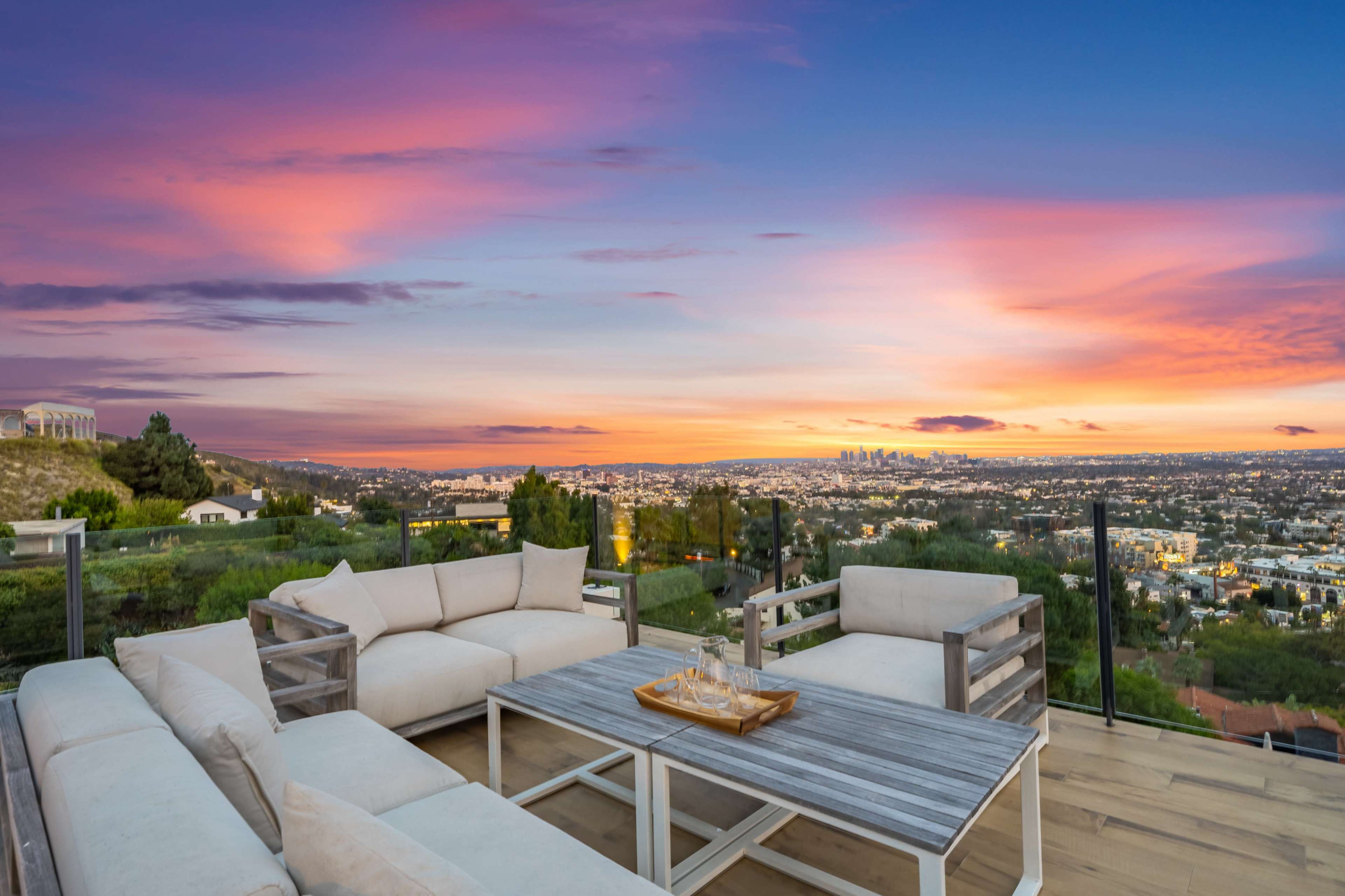 A modern outdoor seating area overlooks a city skyline at sunset.