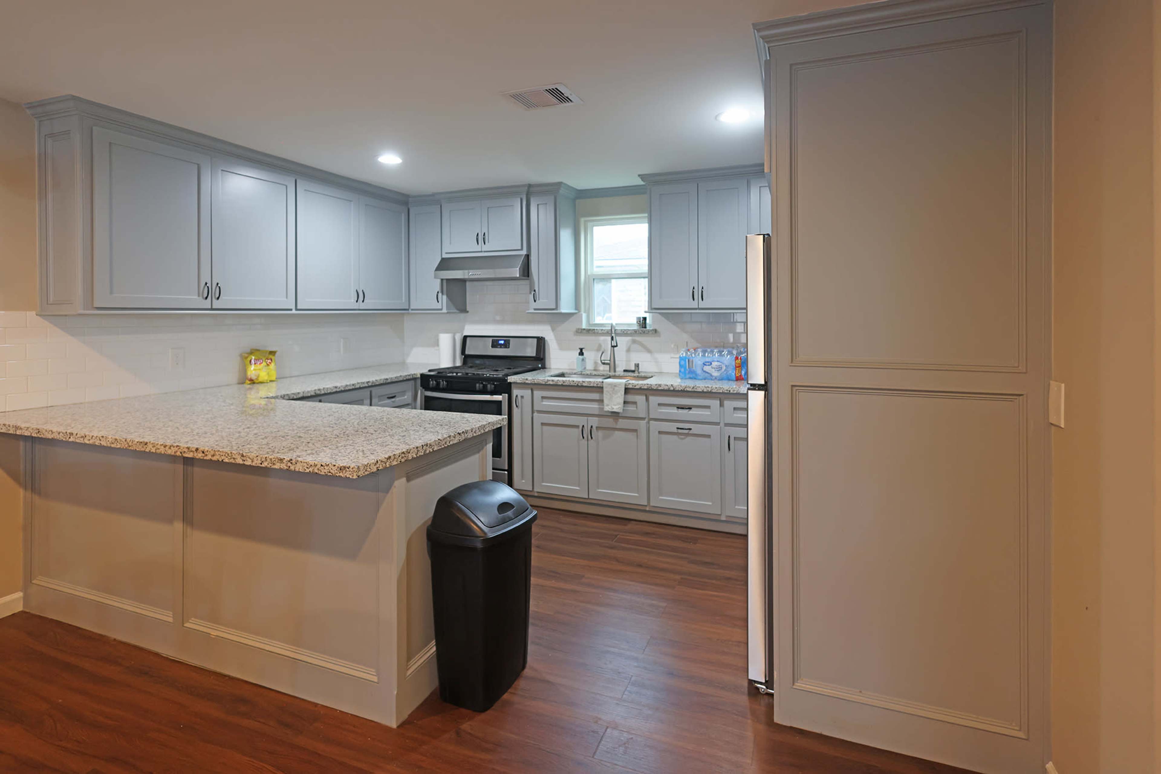 A modern kitchen with gray cabinets, a black stove, and a countertop with a granite surface, featuring wood-like flooring.