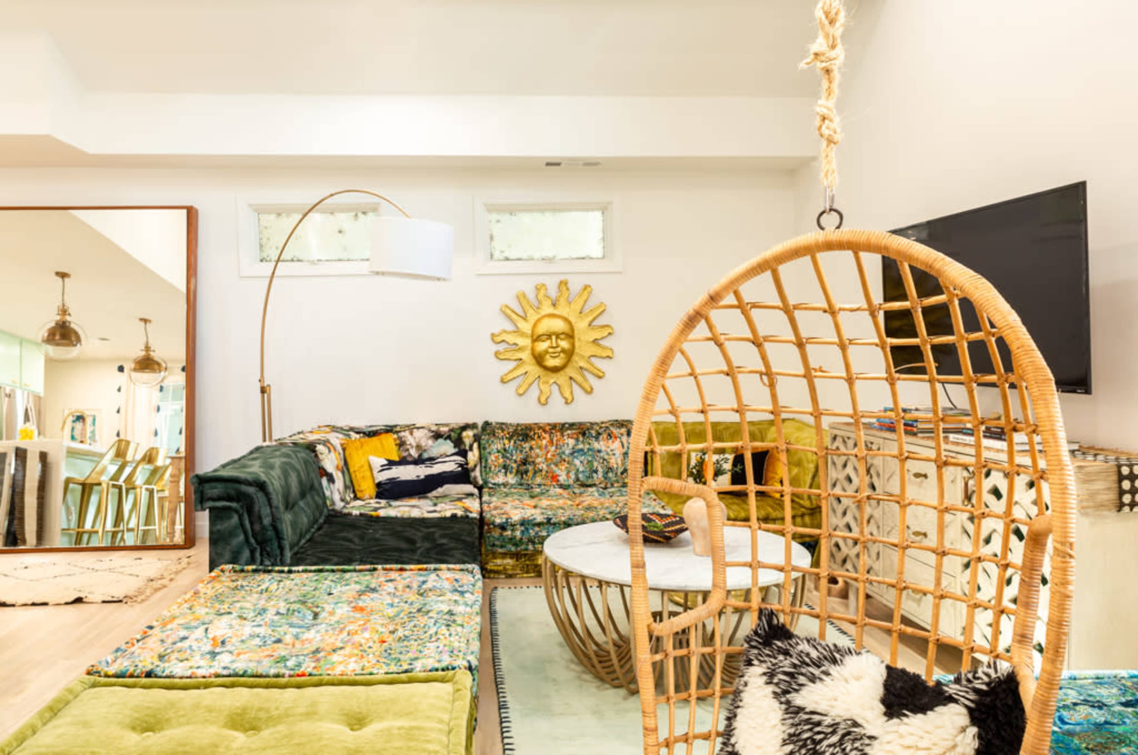 A living room with a large sectional sofa, a round coffee table, a hanging chair, and a sun-shaped wall decoration.