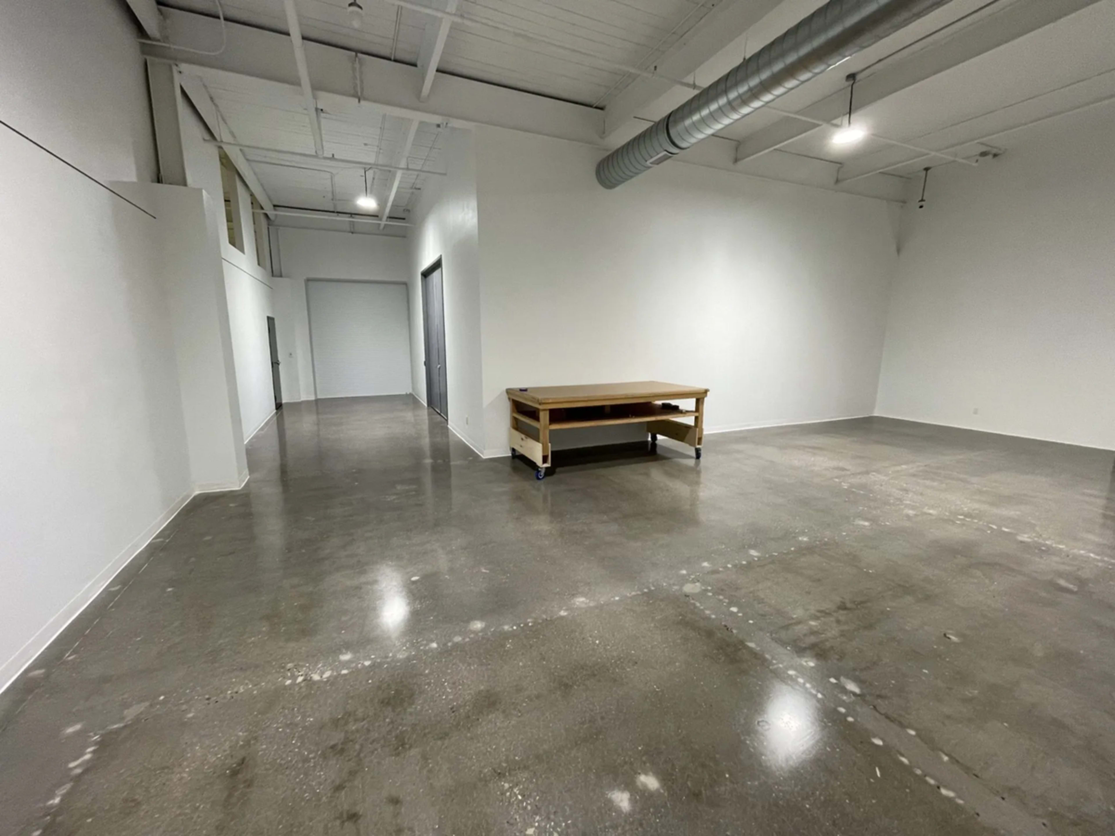 The image shows an empty, spacious interior with polished concrete floors and a wooden table in the center.