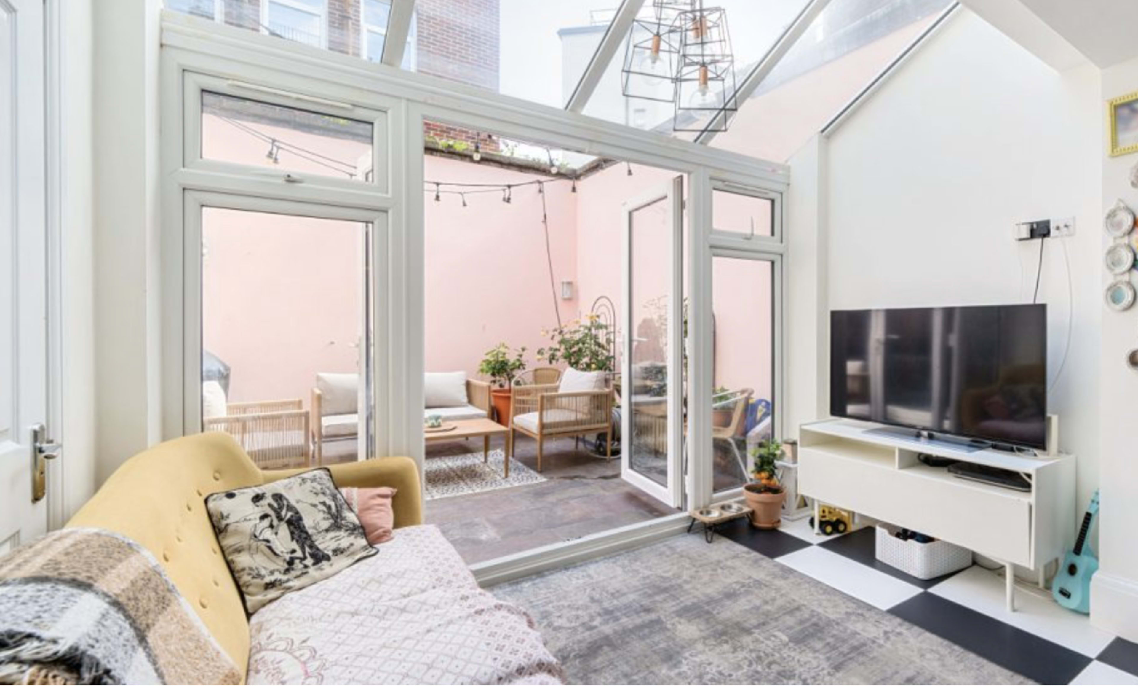 A bright living room features large glass doors that open to a small courtyard with outdoor seating and plants.