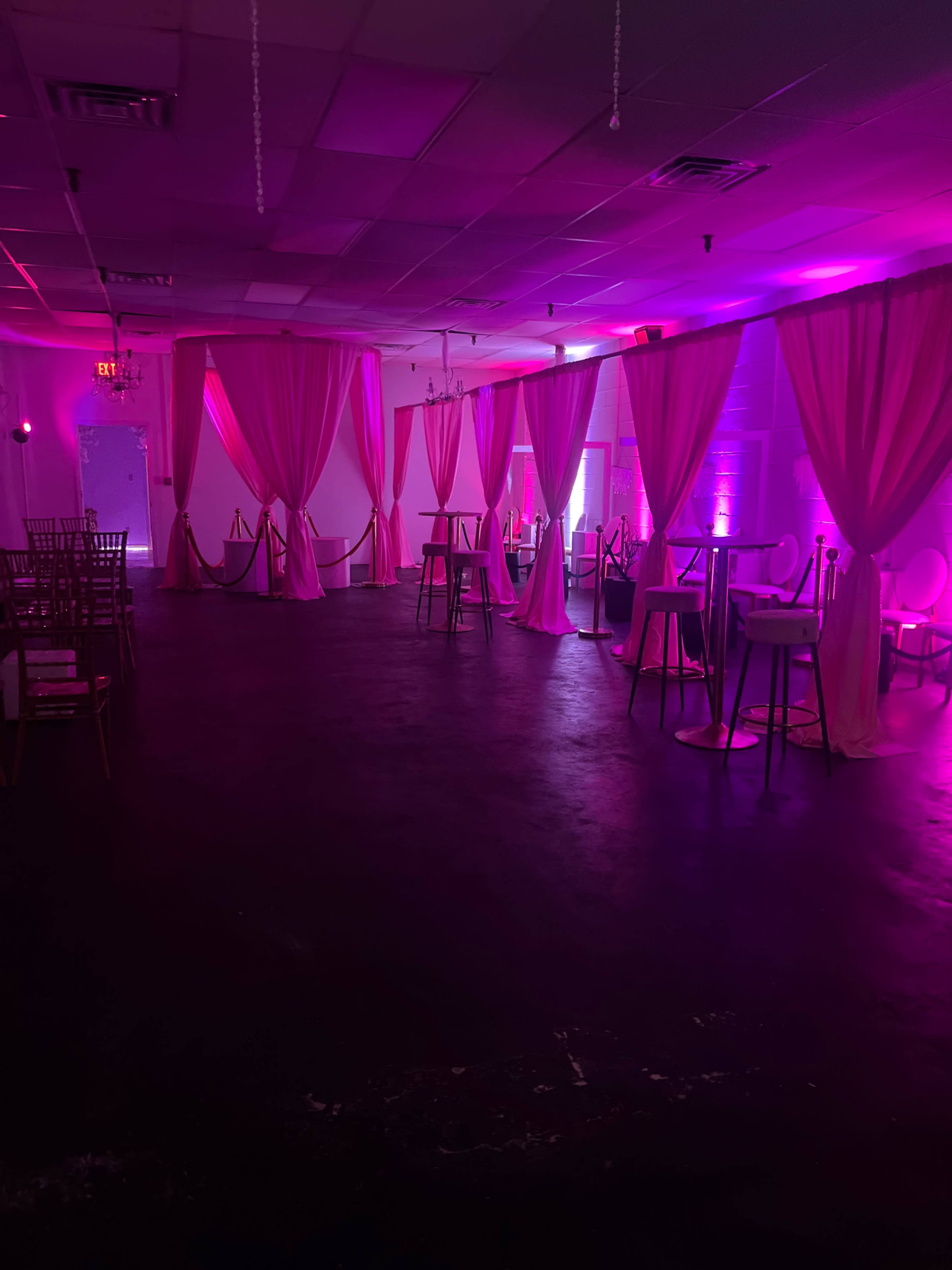 An event space with pink drapery, high tables, and ambient lighting.