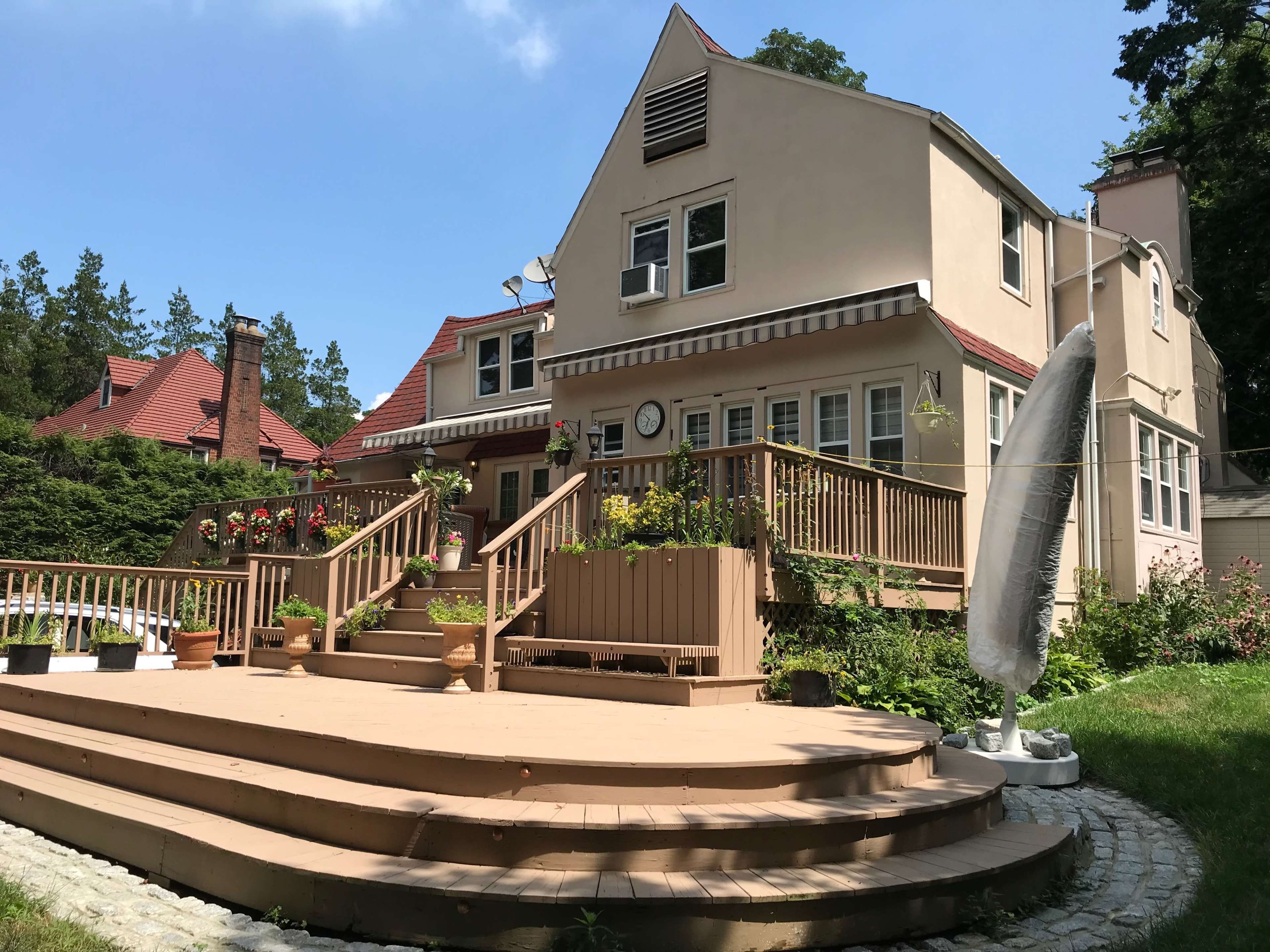 A two-story house with a wooden deck and garden features, surrounded by trees and other homes.