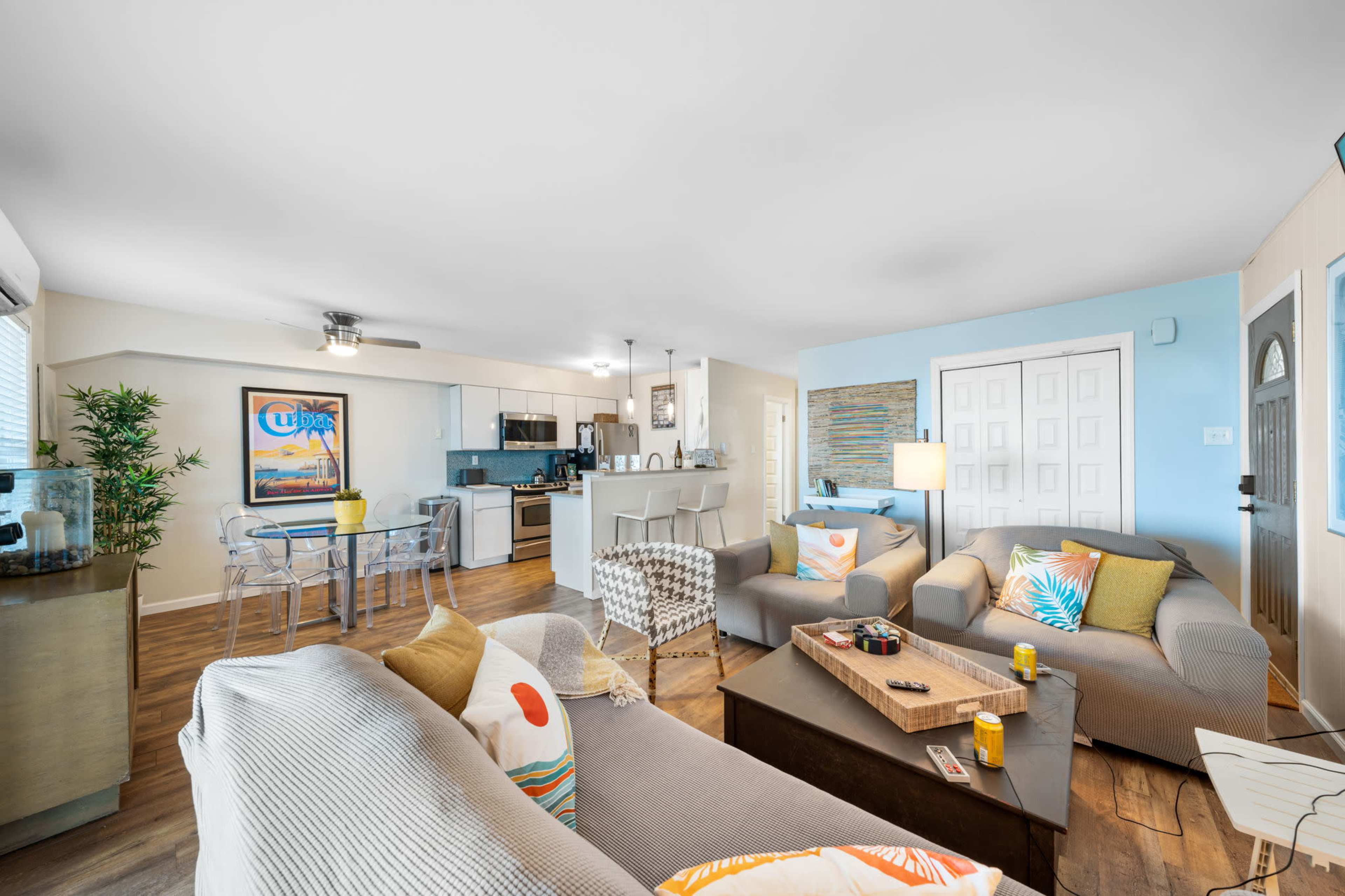 A brightly lit living area features a mix of comfortable seating, a dining space, and a modern kitchen.