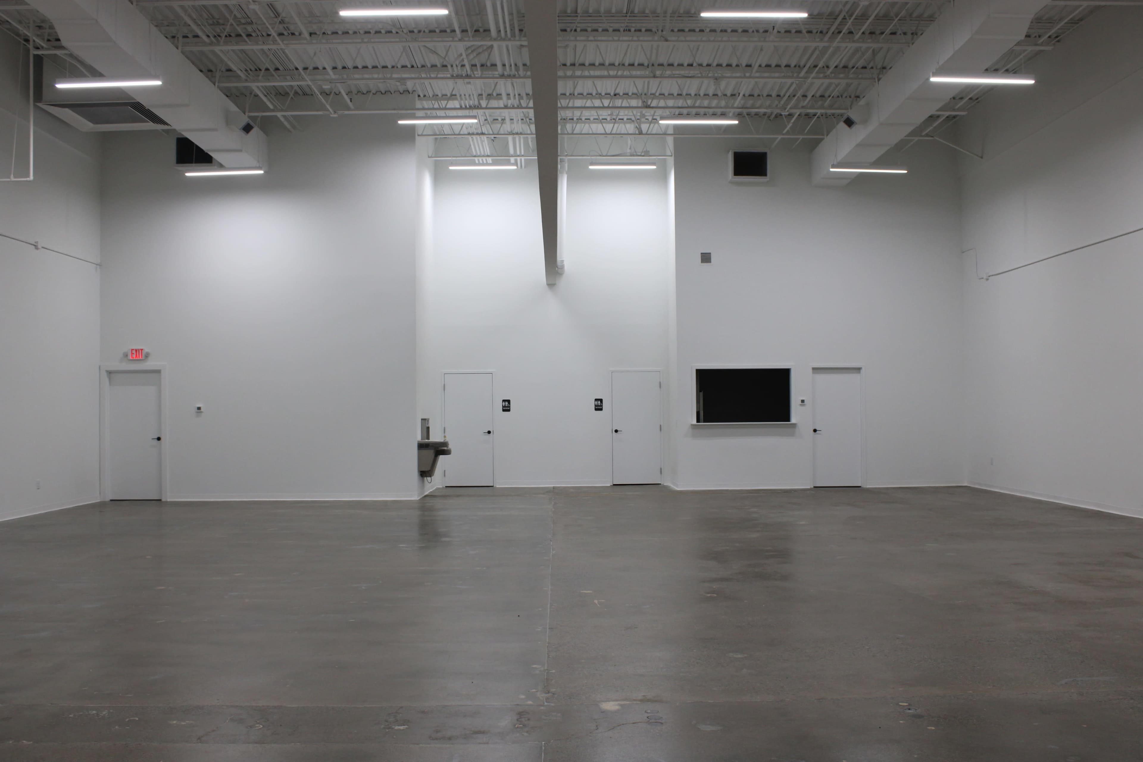 A large, empty interior space with white walls, a concrete floor, and two closed doors.