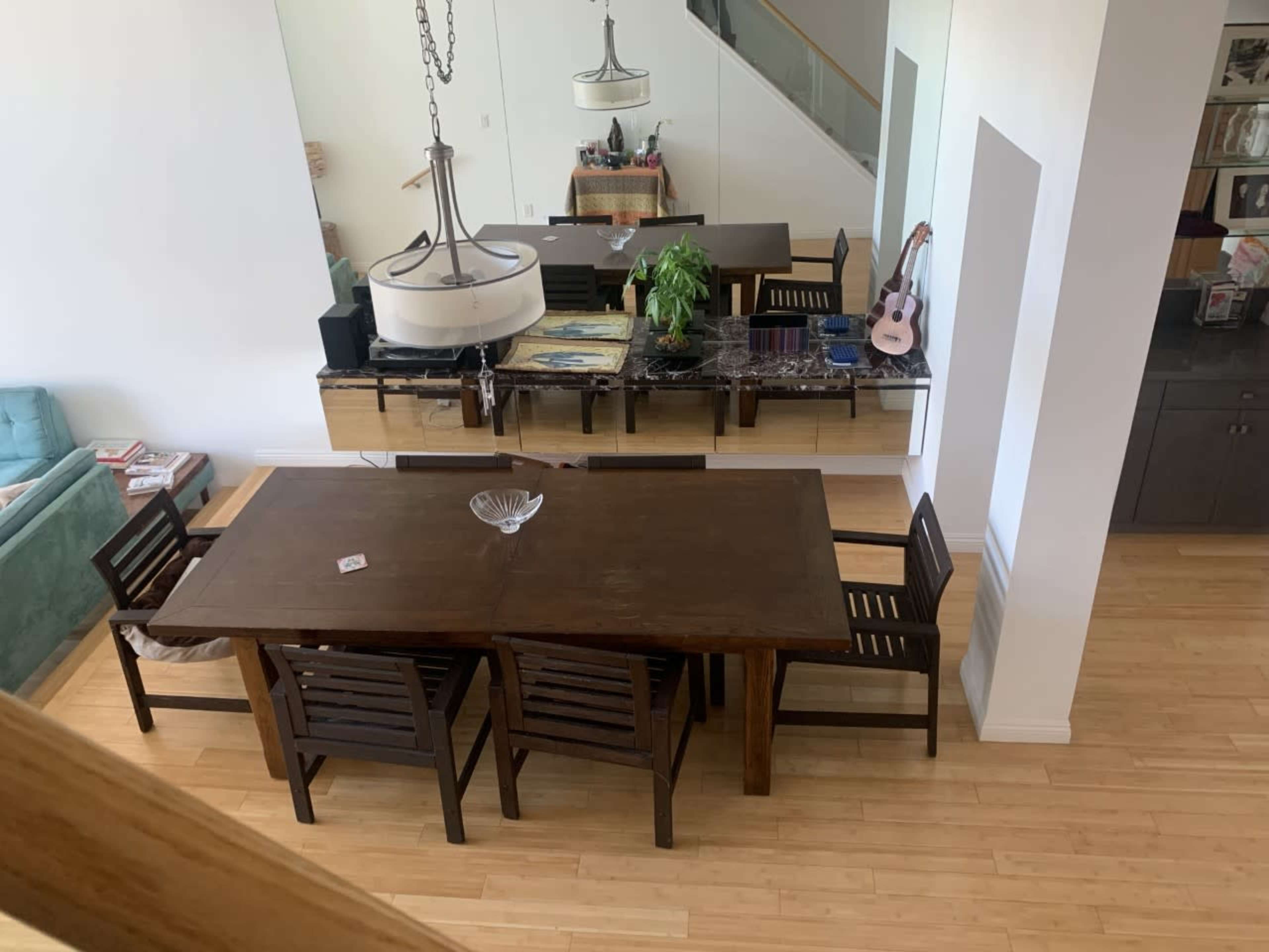 A spacious dining area features a large wooden table surrounded by chairs, with a modern chandelier above and a sideboard displaying decor and plants.