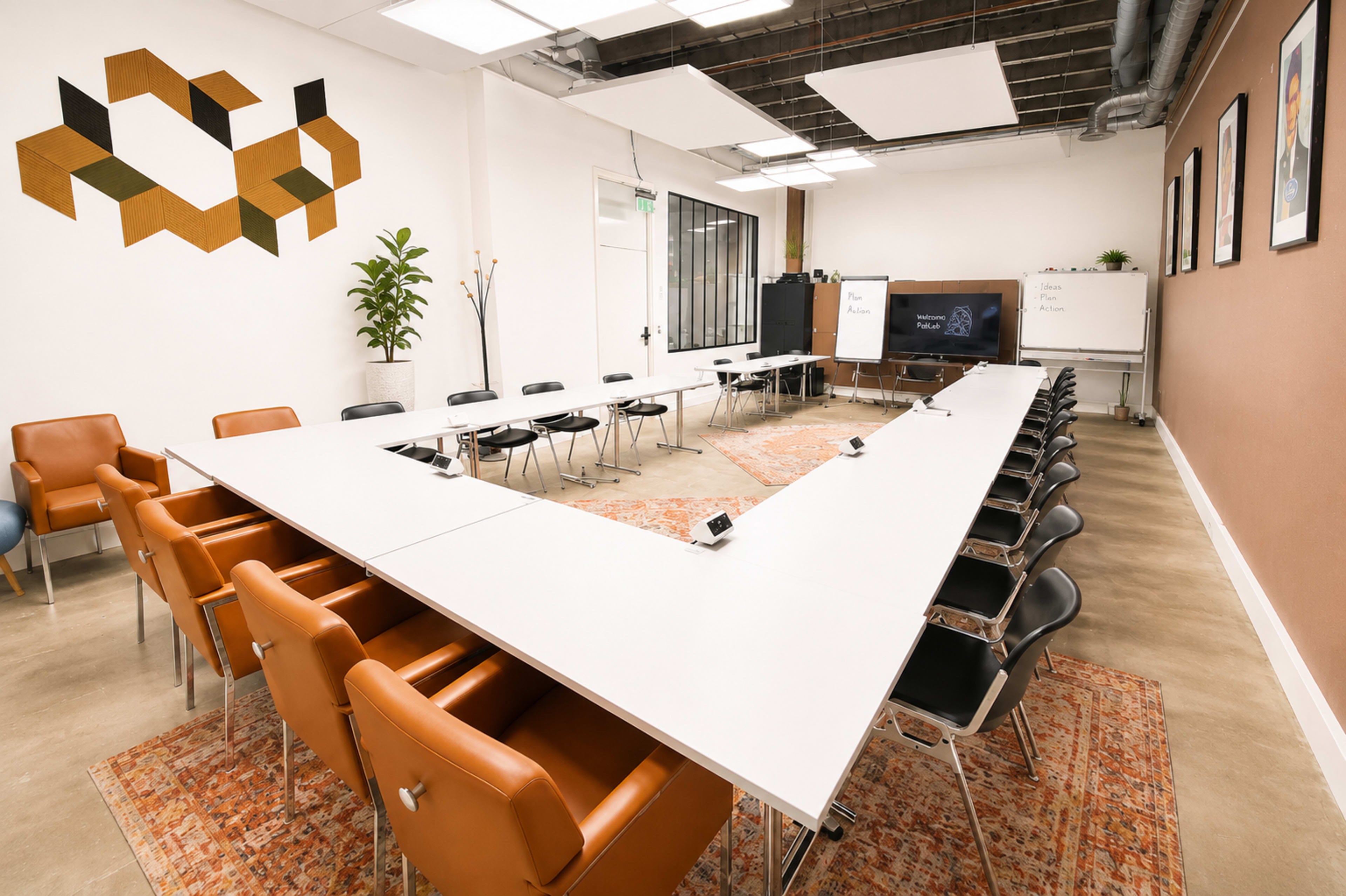The image shows a modern conference room with a large, angled table surrounded by chairs, whiteboards on either side, and decorative wall art.