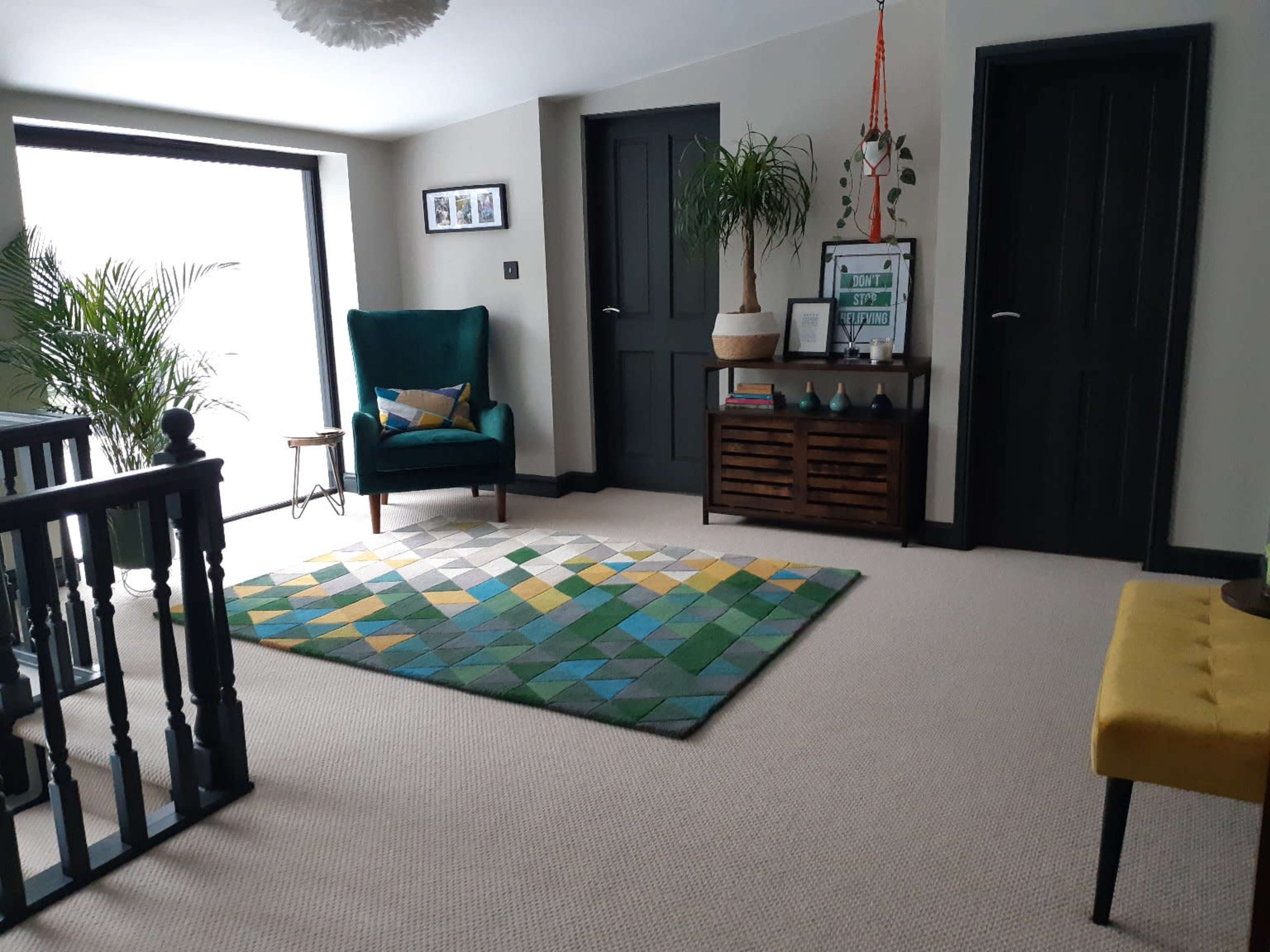 A well-lit room featuring a green armchair, a geometric patterned rug, a console table, and two doors against a neutral wall.