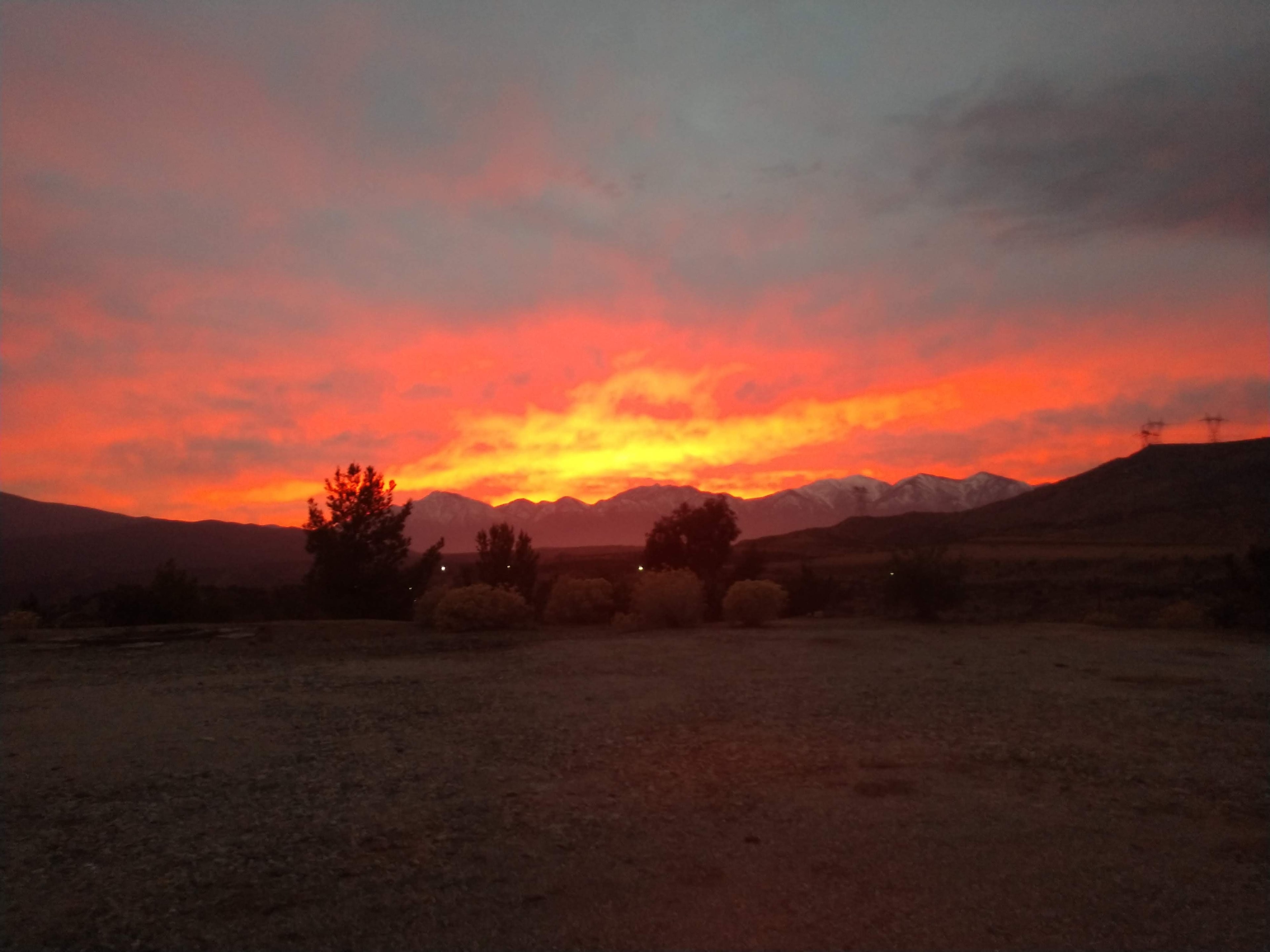 The image shows a vibrant sunset over a mountainous landscape, with trees and shrubbery in the foreground.