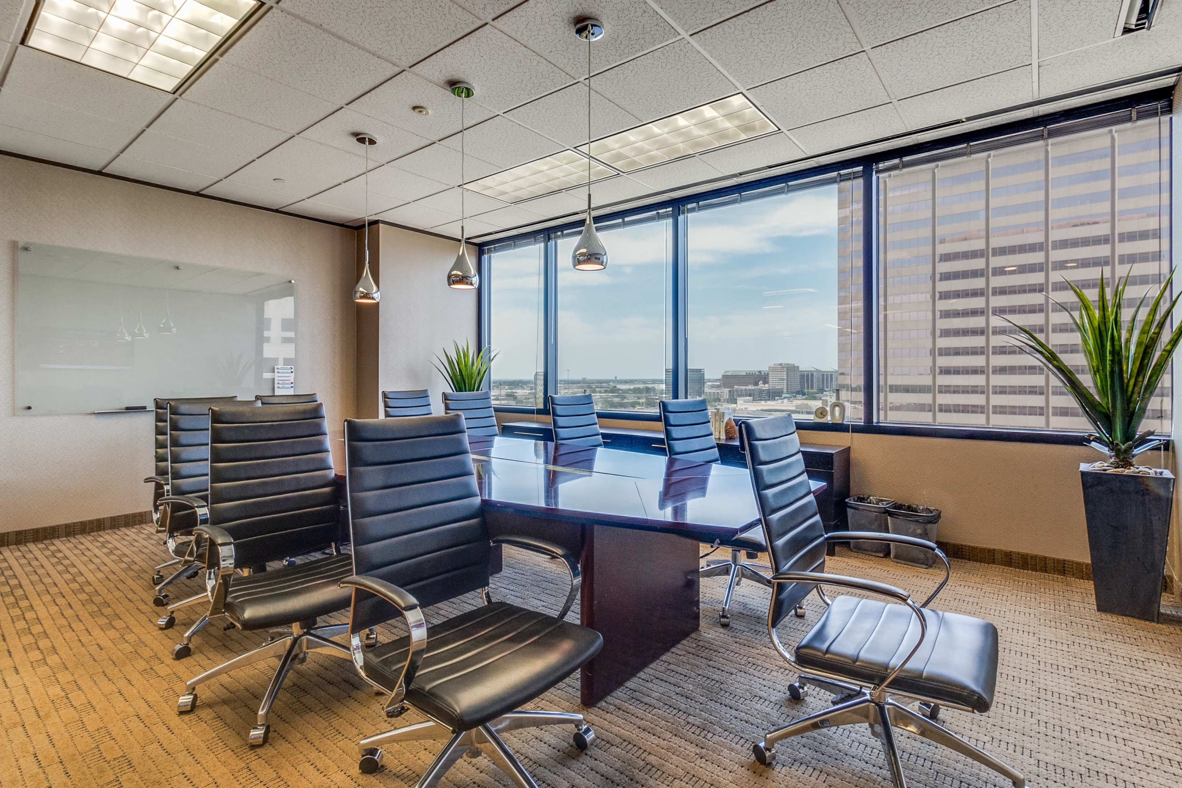 A modern conference room features a large wooden table surrounded by black leather chairs, with windows providing a view of the city skyline.