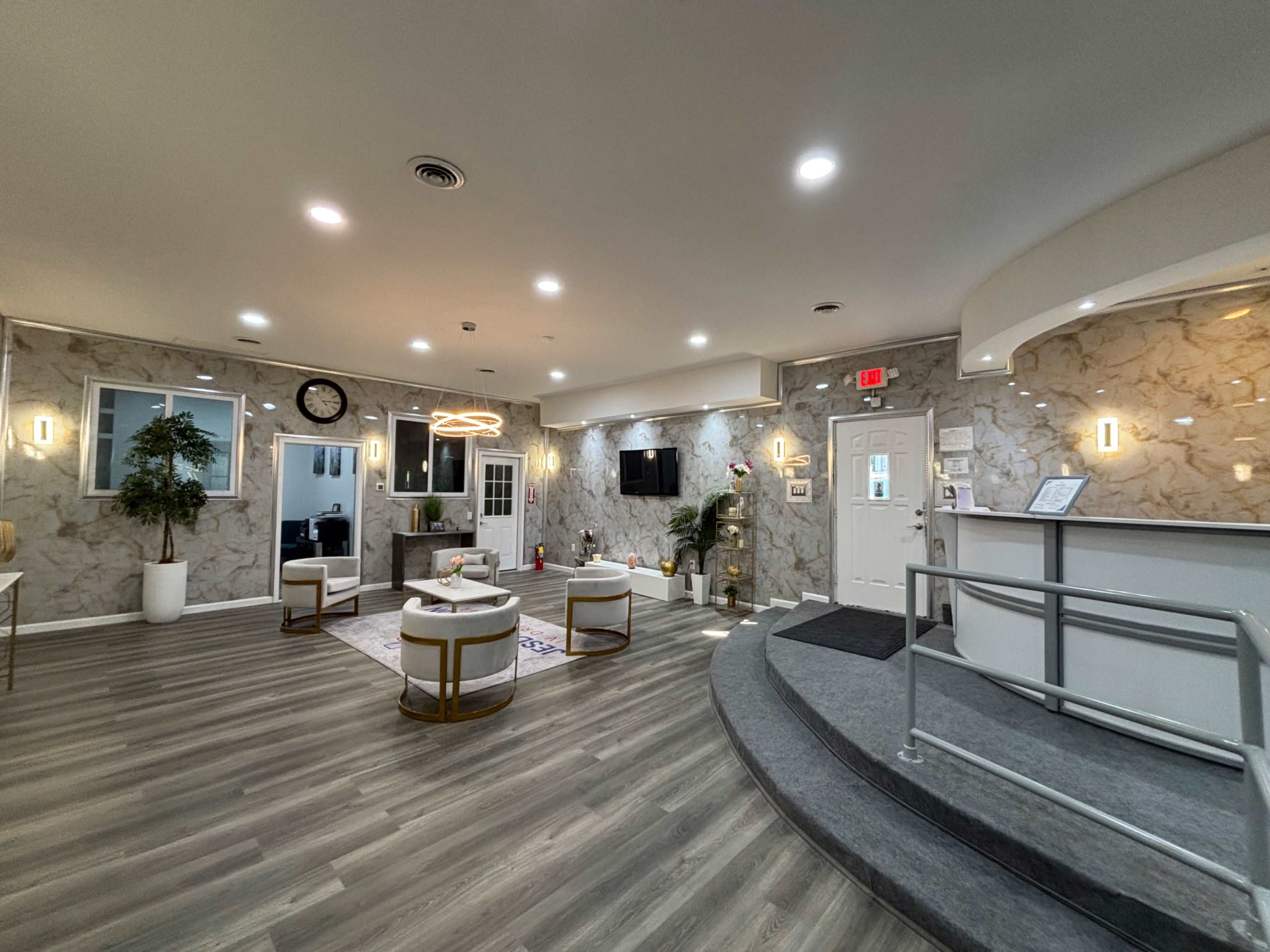 The image shows a modern reception area with sleek furnishings, a decorative wall, and a front desk.