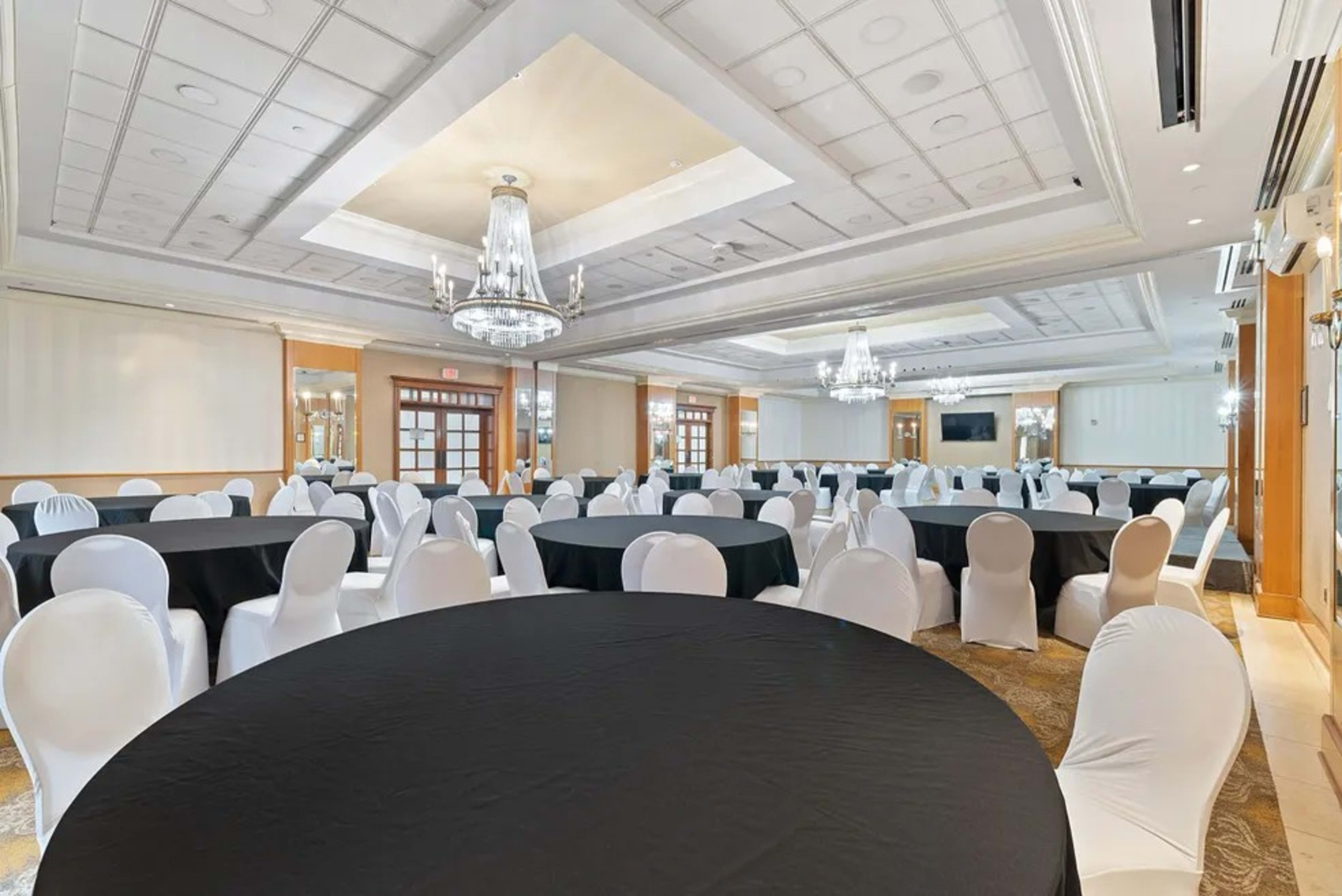 A large event space features multiple round tables covered with black and white tablecloths, all arranged in rows with chandeliers overhead.