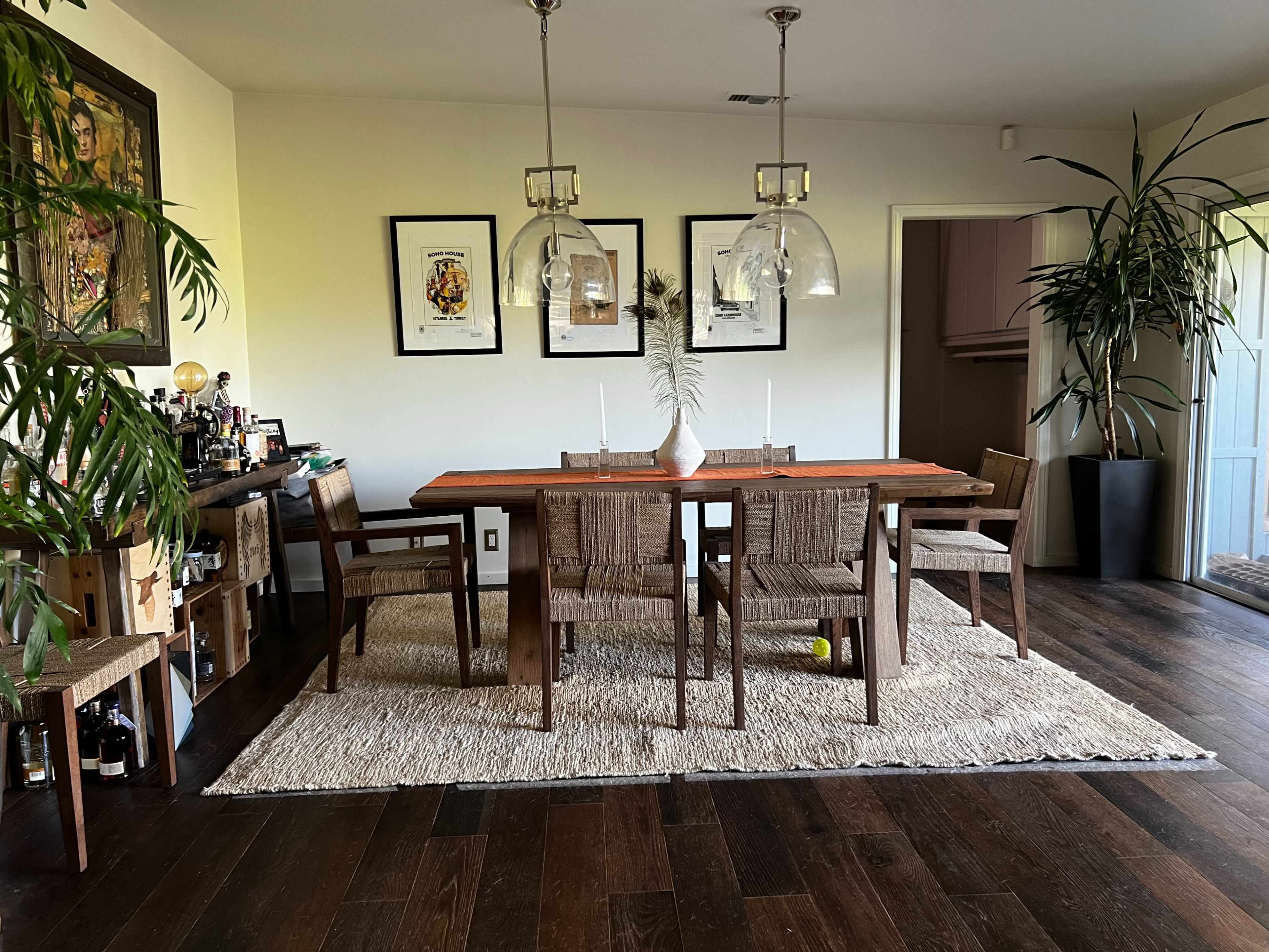 A modern dining room features a wooden table surrounded by chairs, with a large area rug and framed artwork on the walls.
