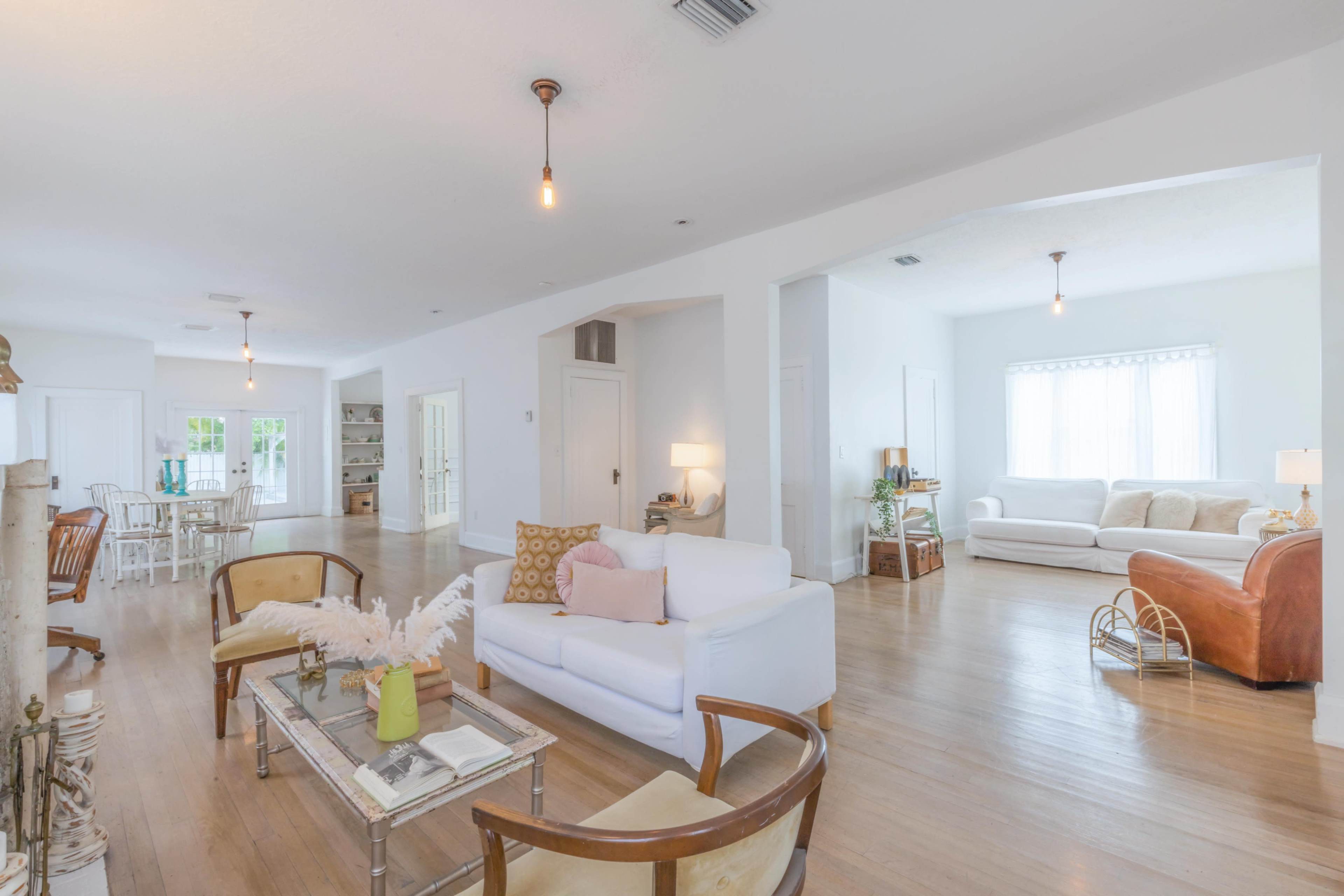 A spacious, bright living area with a combination of seating arrangements including a white sofa, armchairs, and a coffee table, illuminated by pendant lights.
