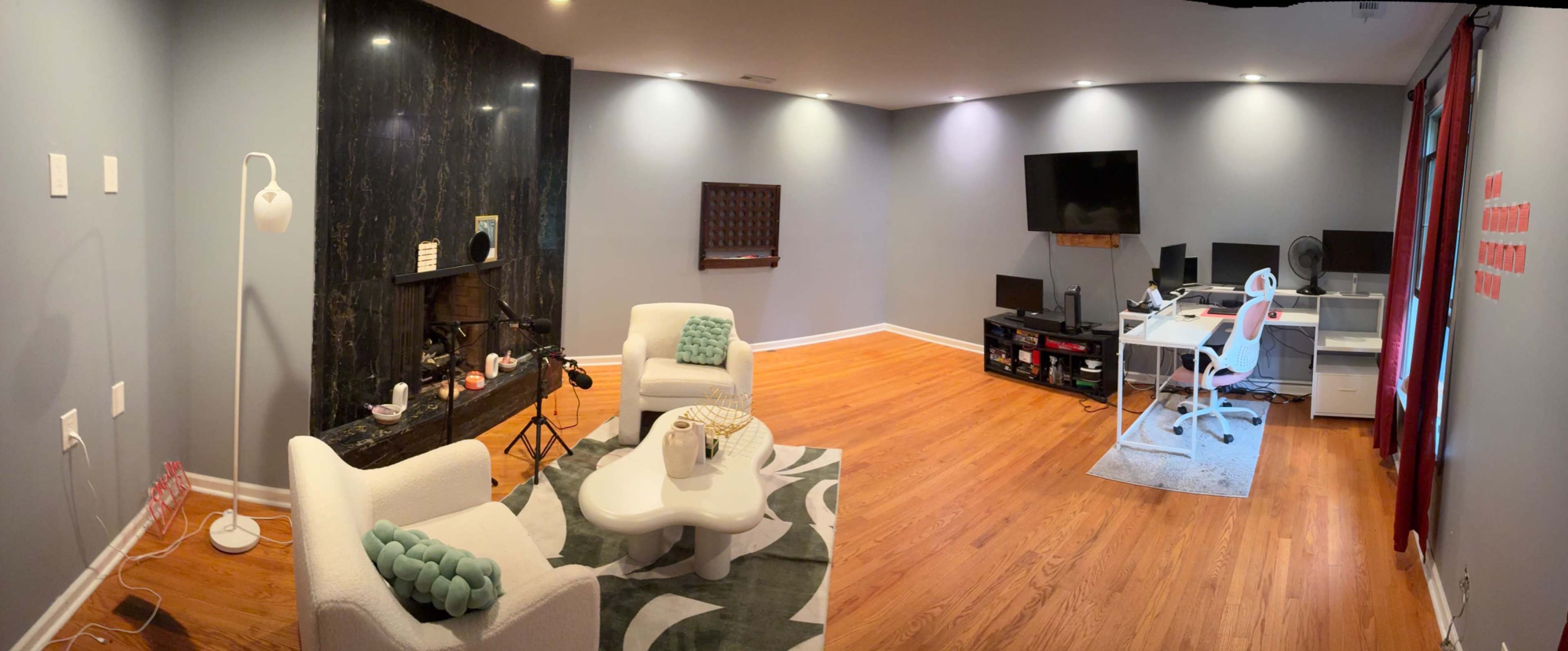 The image shows a spacious, modern living area with two white chairs and a coffee table, a desk with a computer setup, and a large flat-screen TV mounted on the wall.