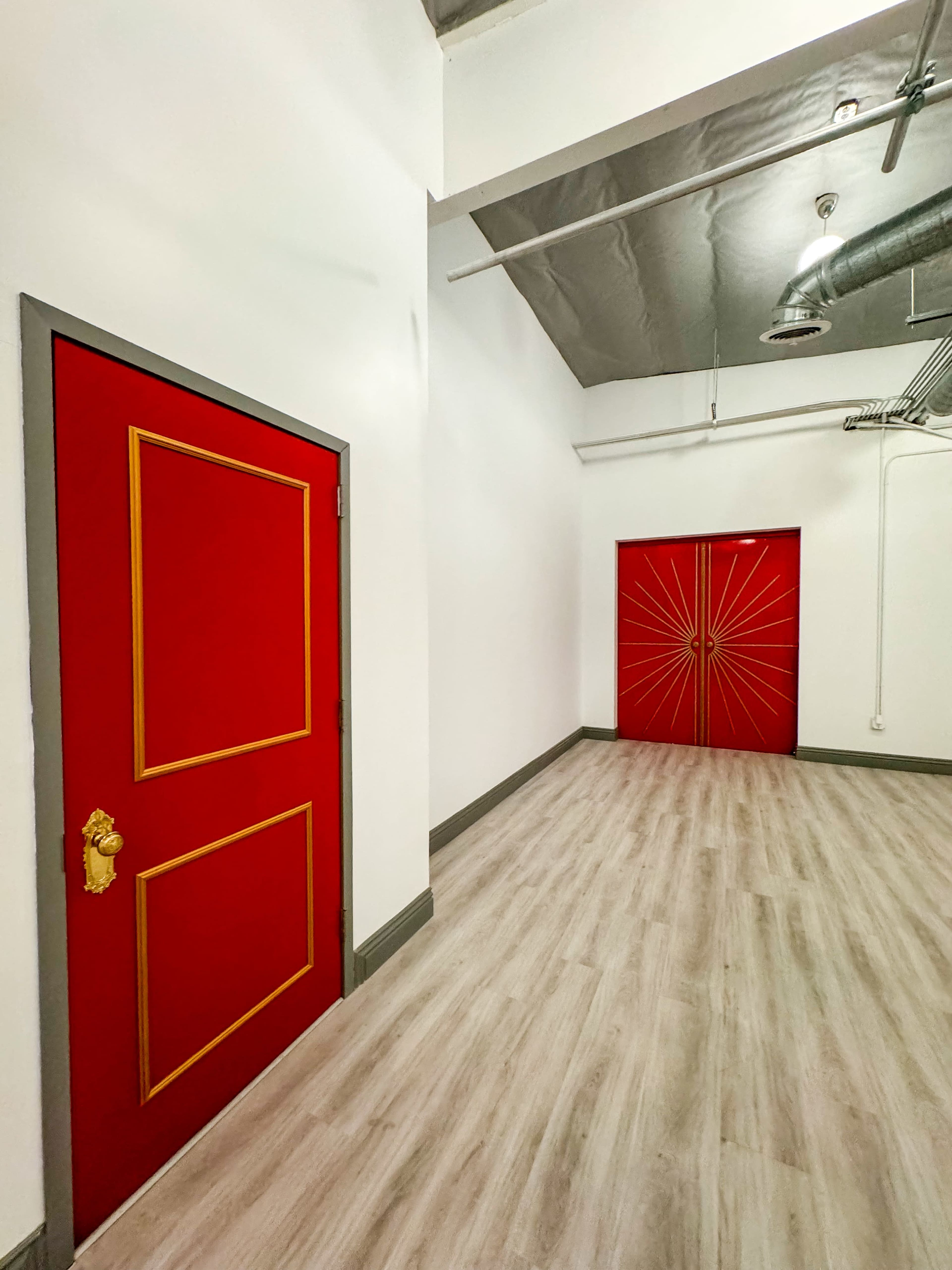 A spacious hallway with two red doors at the end, one featuring a simple frame and the other adorned with a sunburst design.