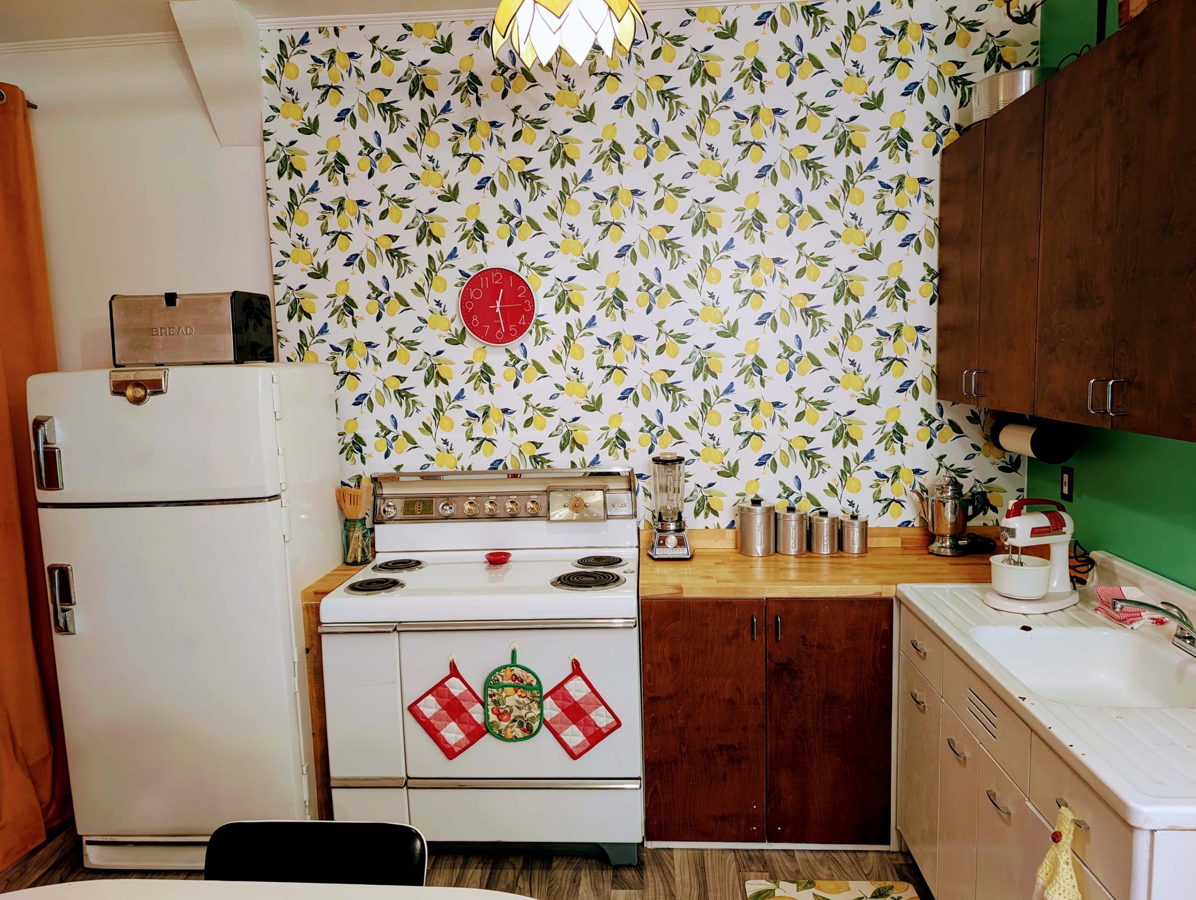 A retro kitchen features a white stove, a vintage refrigerator, a wood countertop, and a patterned lemon wallpaper.